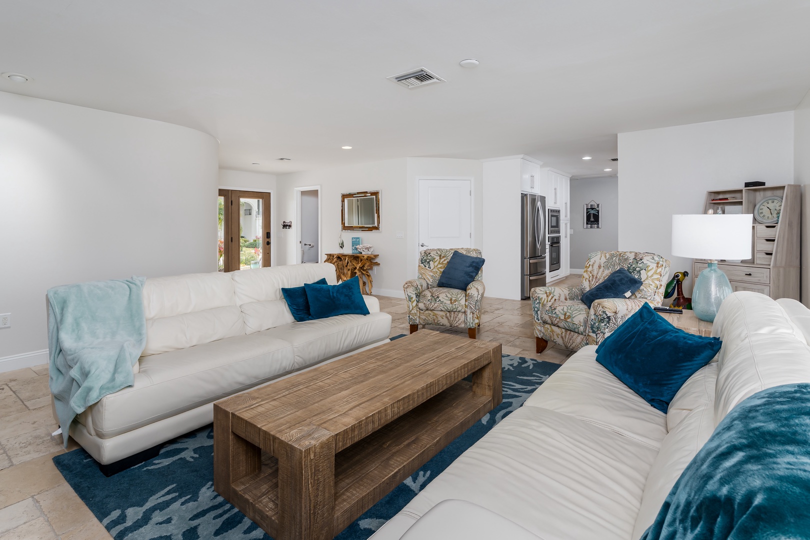 Sink into plush white sofas with ocean-blue accents in your spacious open living area, where natural light flows through French doors.