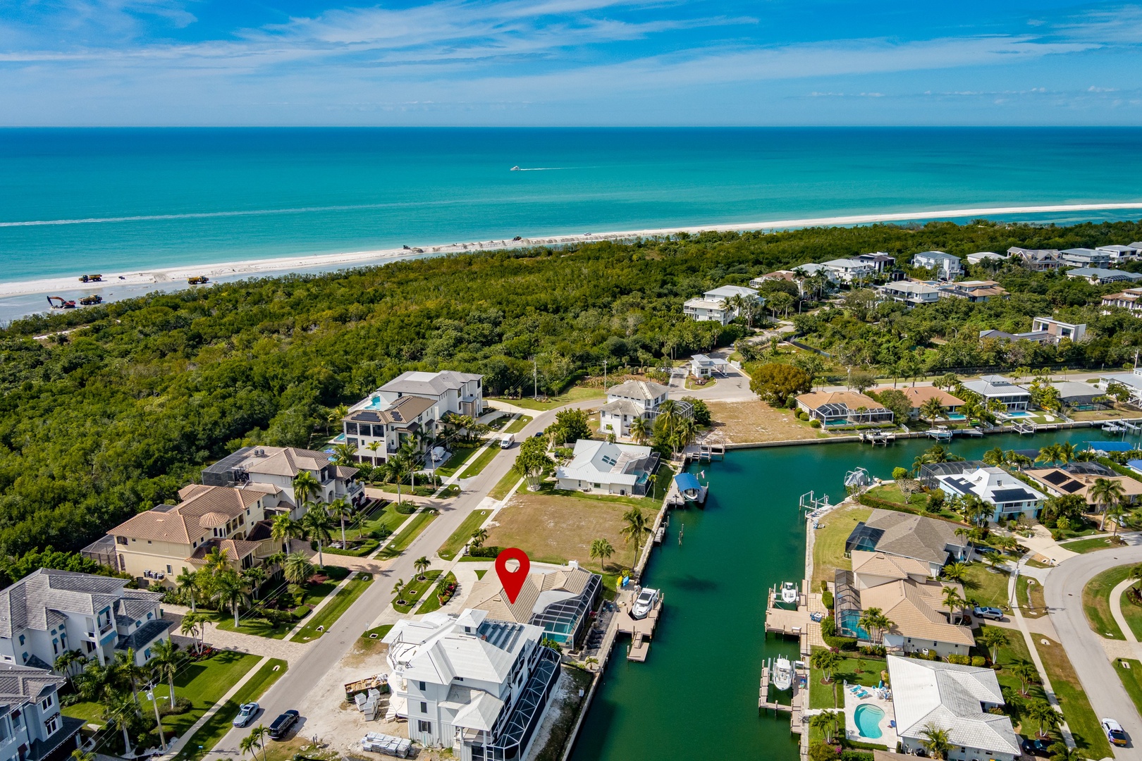Stunning aerial view of waterfront community with canal access and pristine beach beyond lush tropical landscape.