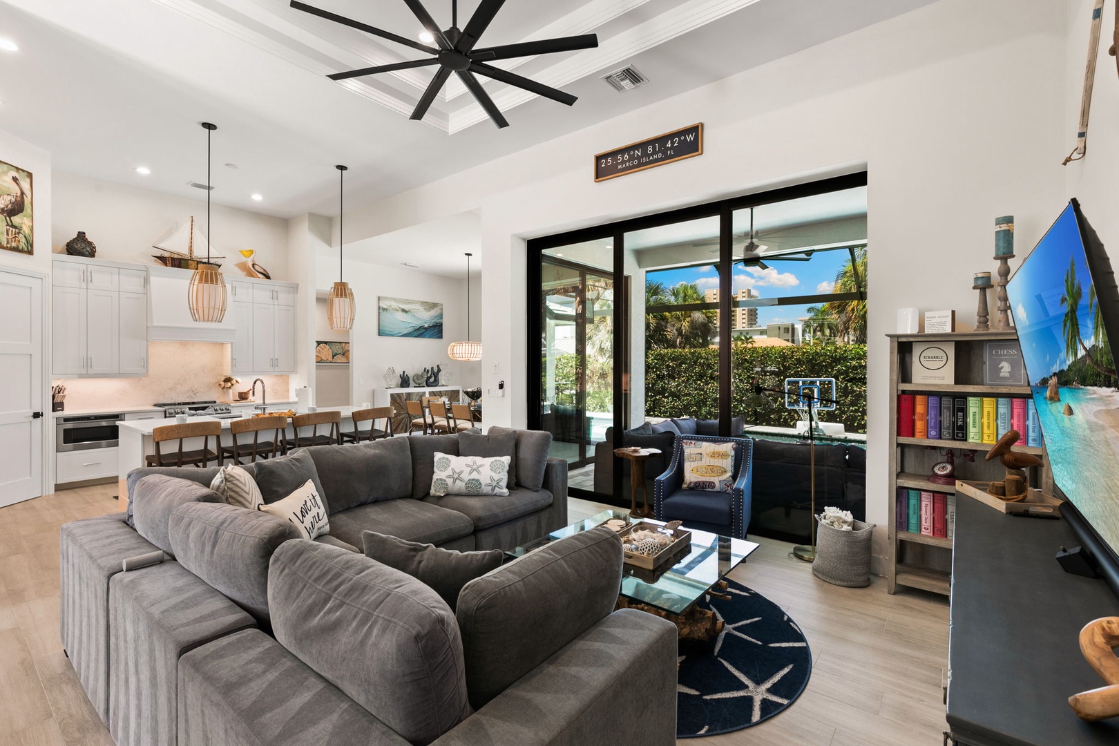 Open-concept living room with soaring ceilings, plush sectional seating, and floor-to-ceiling glass doors flooding the space with natural light and tropical breezes.