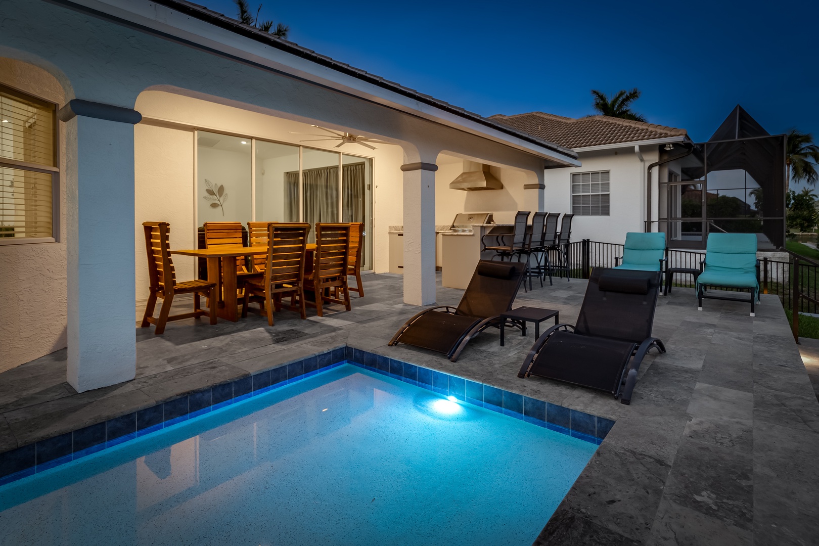 Modern vacation home exterior featuring a private pool, covered patio with outdoor dining, and multiple lounge areas perfect for evening relaxation under tropical skies.