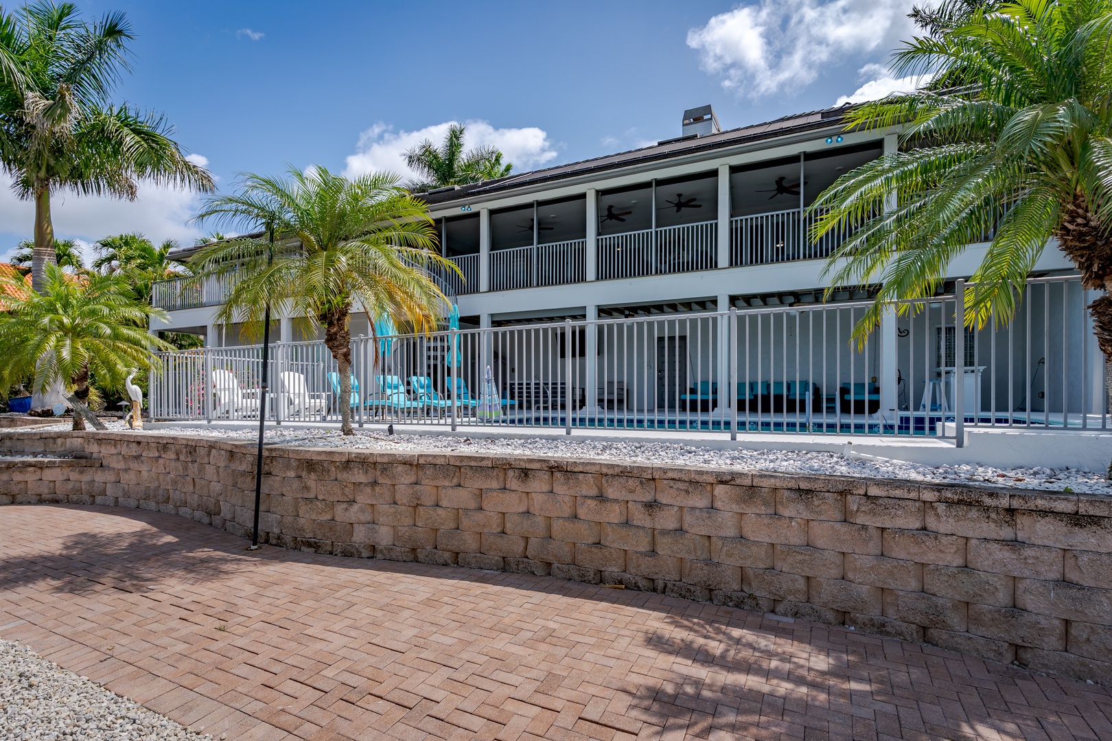The property features a two-story structure with expansive balconies, framed by tropical palm trees and a decorative stone-bordered patio area leading to a pool.