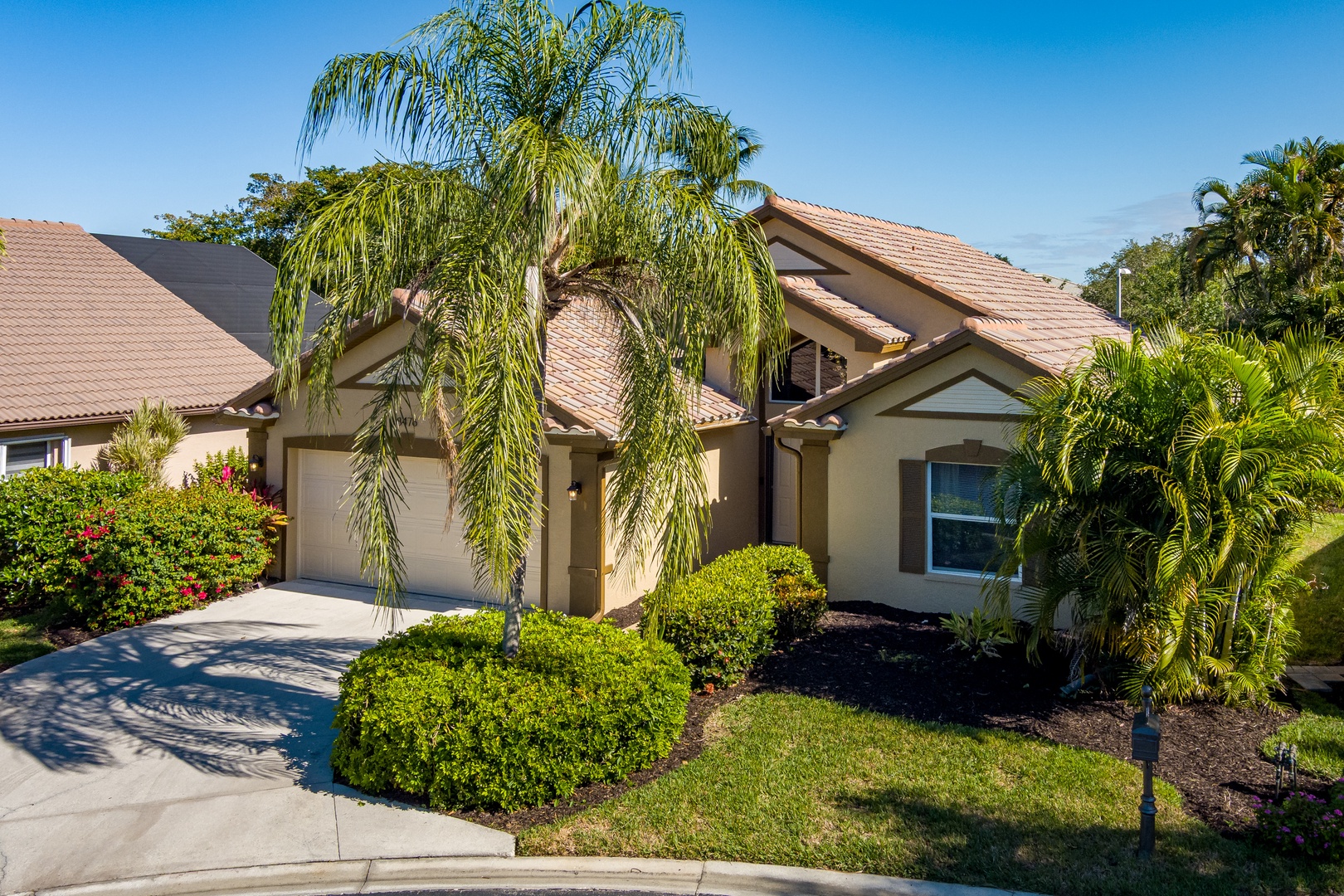 A beautiful single-story home with tile roof and tropical landscaping featuring mature palm trees and manicured gardens.