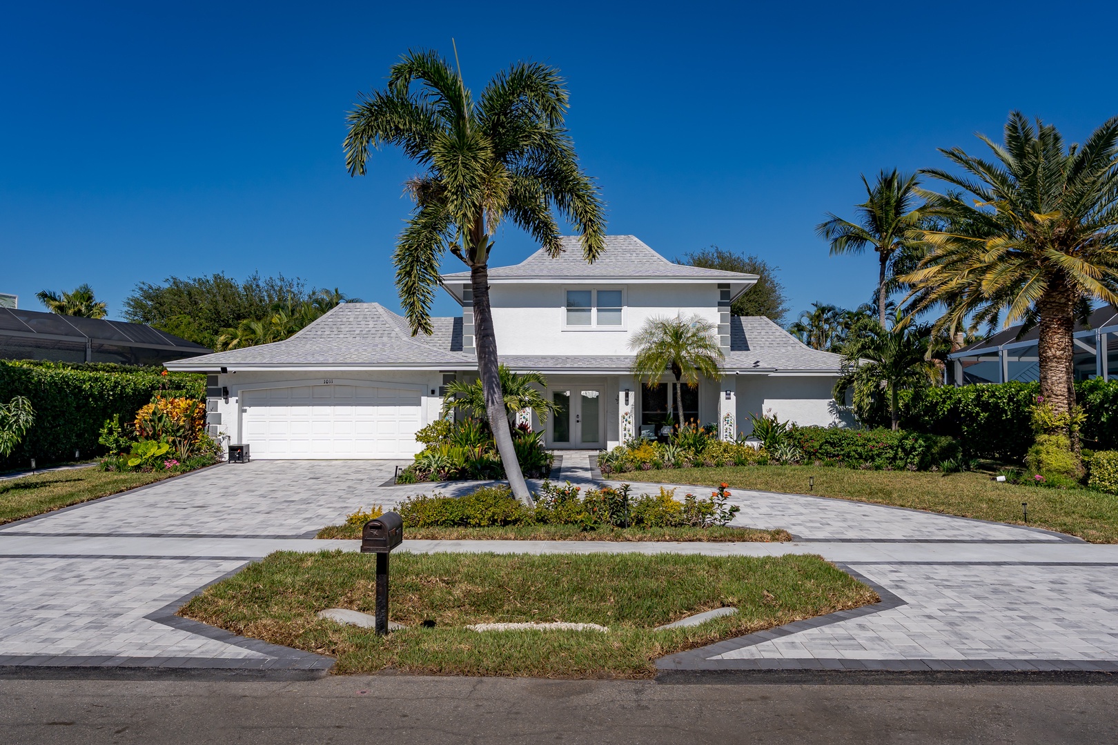 Modern white vacation home surrounded by tropical palm trees and lush landscaping in a peaceful residential setting.