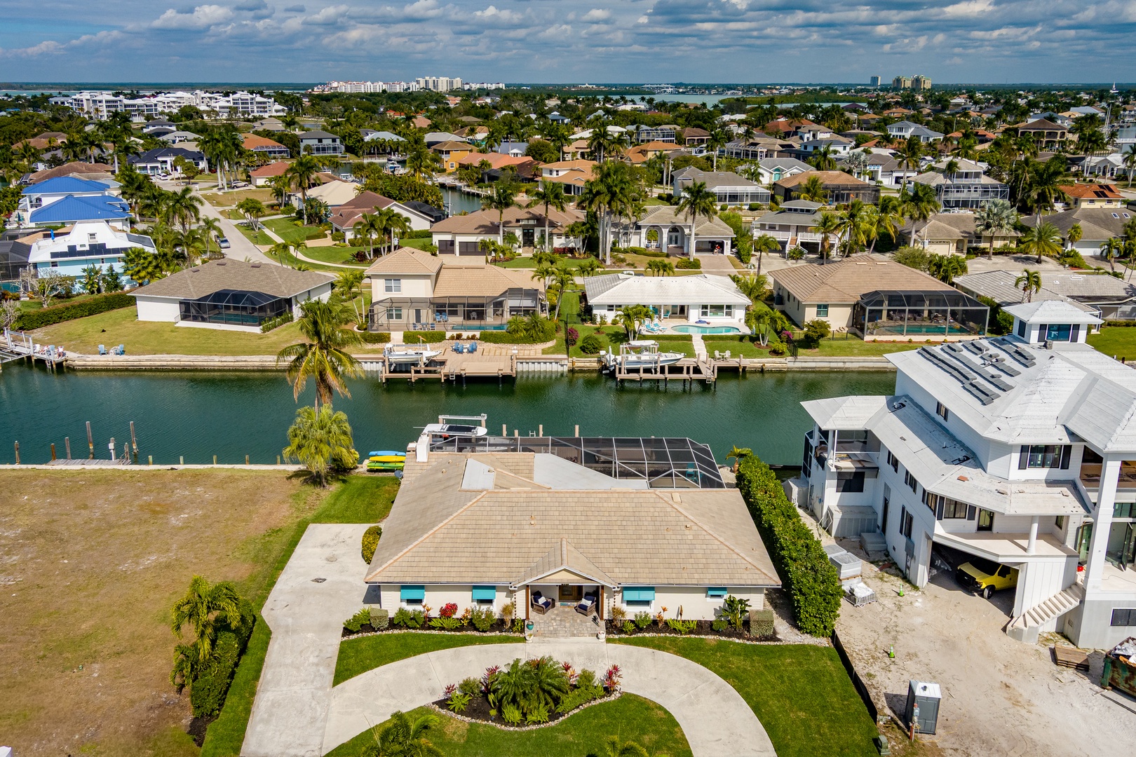 Aerial view showcasing a waterfront property surrounded by manicured landscaping in a pristine residential neighborhood with canal access and tropical setting.