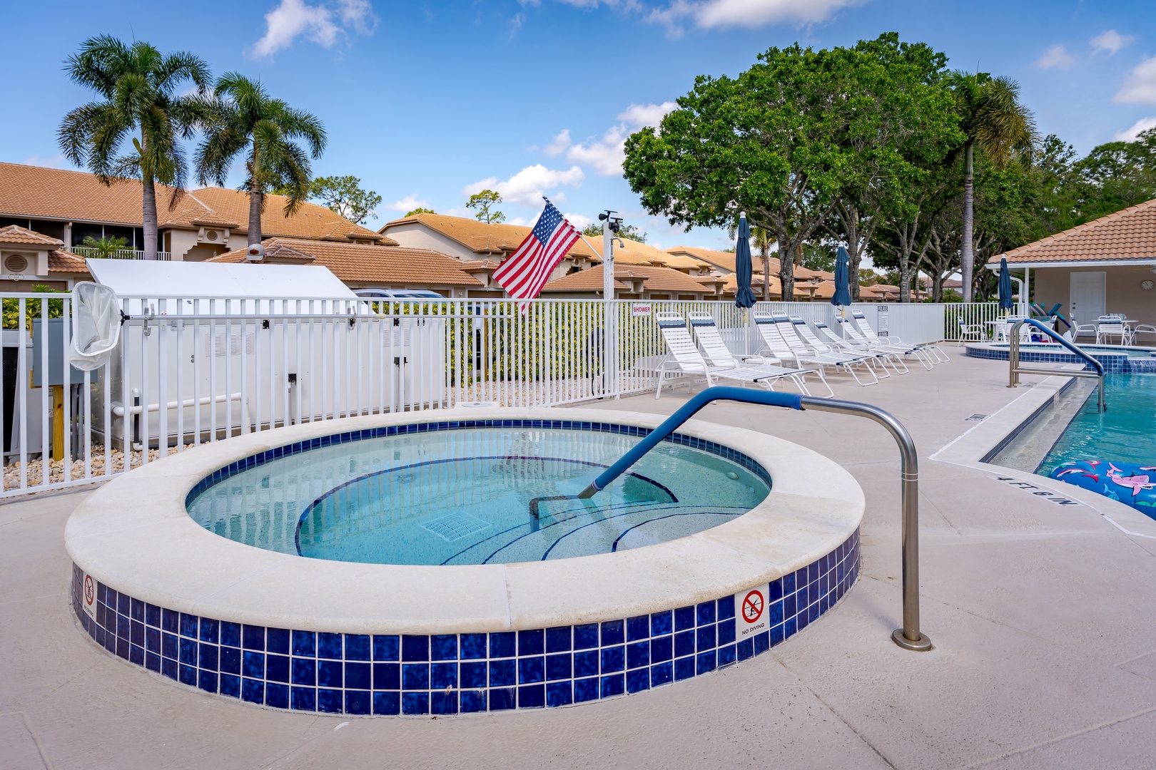 A circular hot tub with blue tile trim sits beside the main pool, surrounded by lounge chairs under a sunny Florida sky—your perfect spot to unwind after a day of adventure.