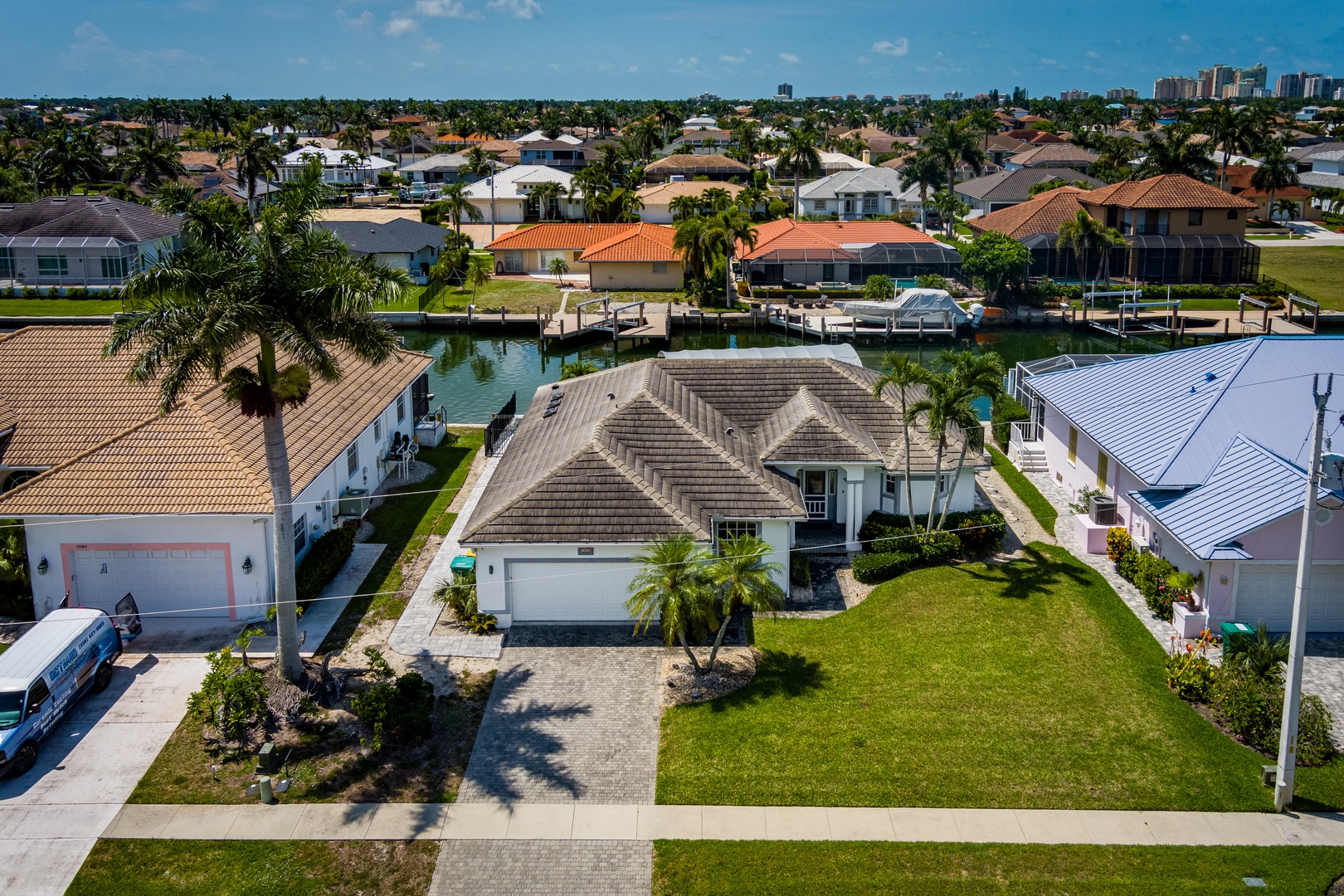 Aerial view of a waterfront vacation rental in a sunny Florida neighborhood with canal access and nearby city skyline views.