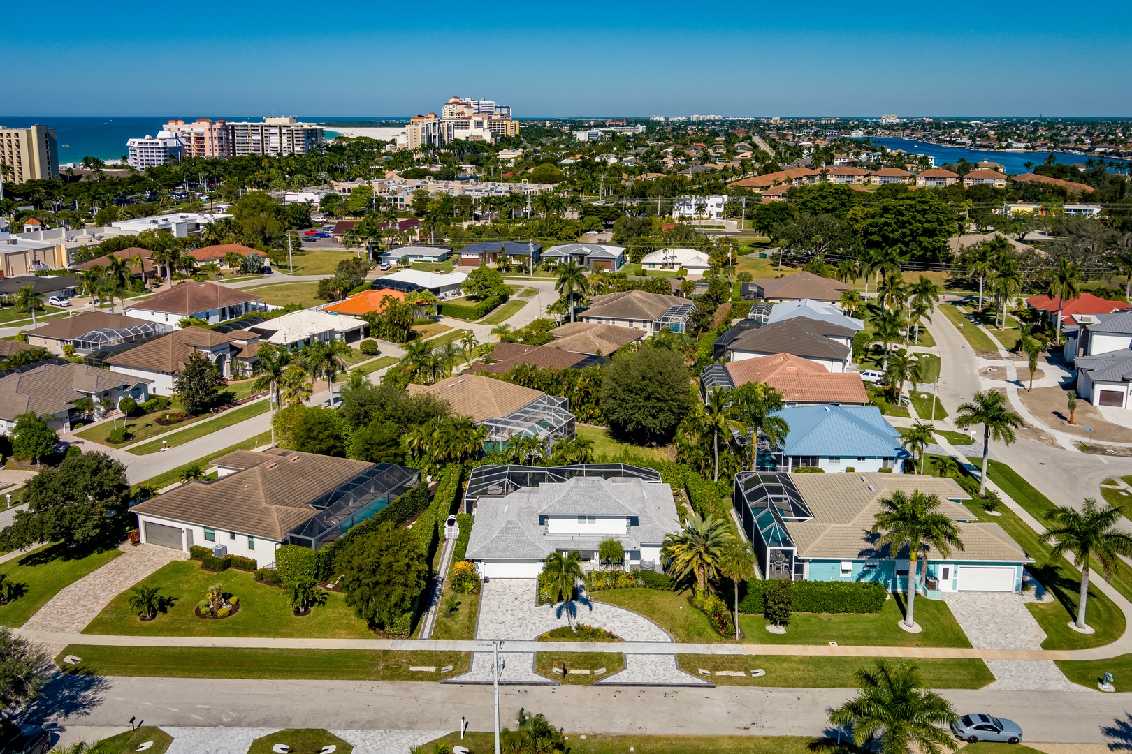 Aerial view of a tropical coastal neighborhood with palm-lined streets, swimming pools, and ocean views in the distance.