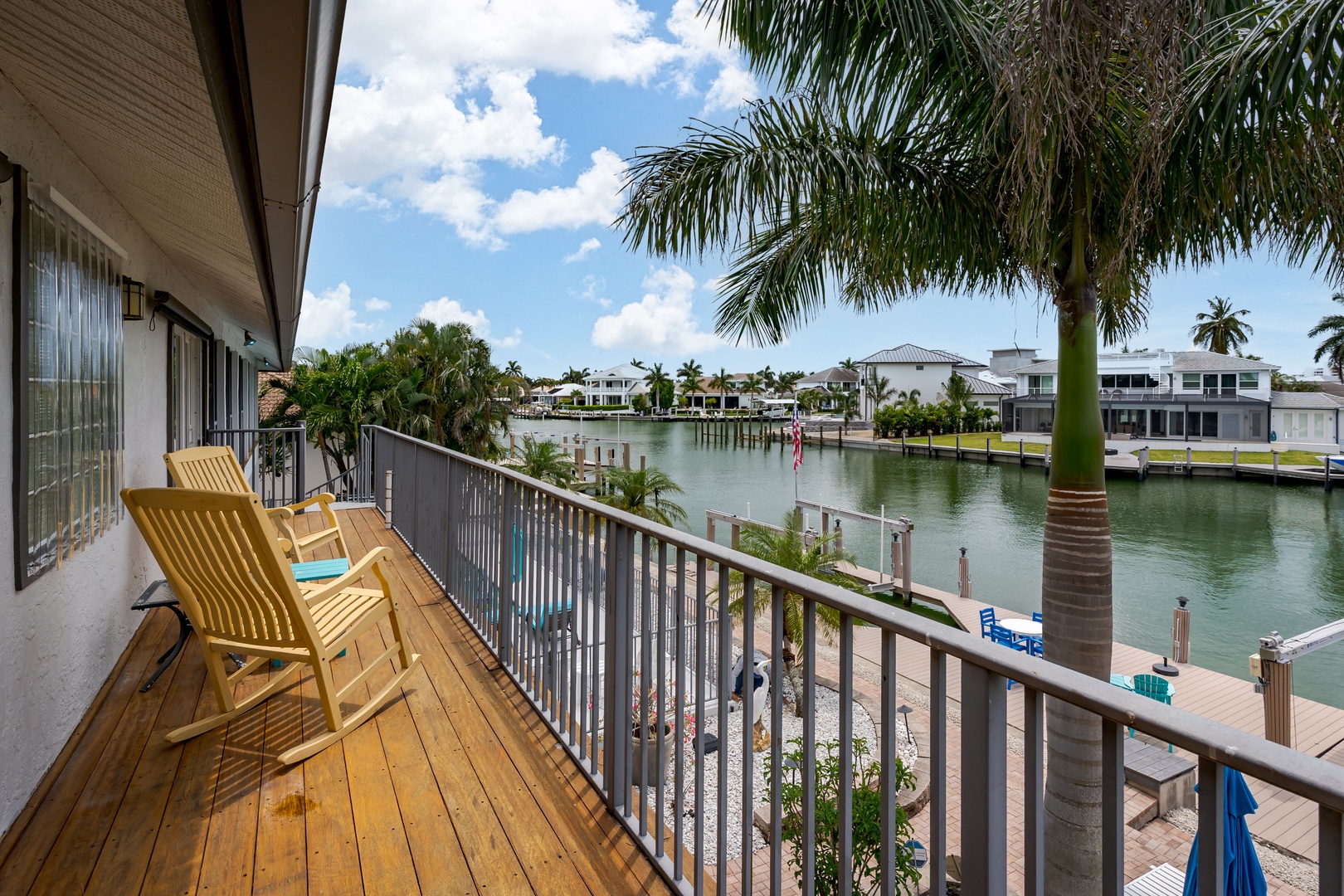 Relax in your lounge chairs on the private balcony, soaking in tranquil canal views framed by swaying palms and coastal homes in this peaceful waterfront setting.