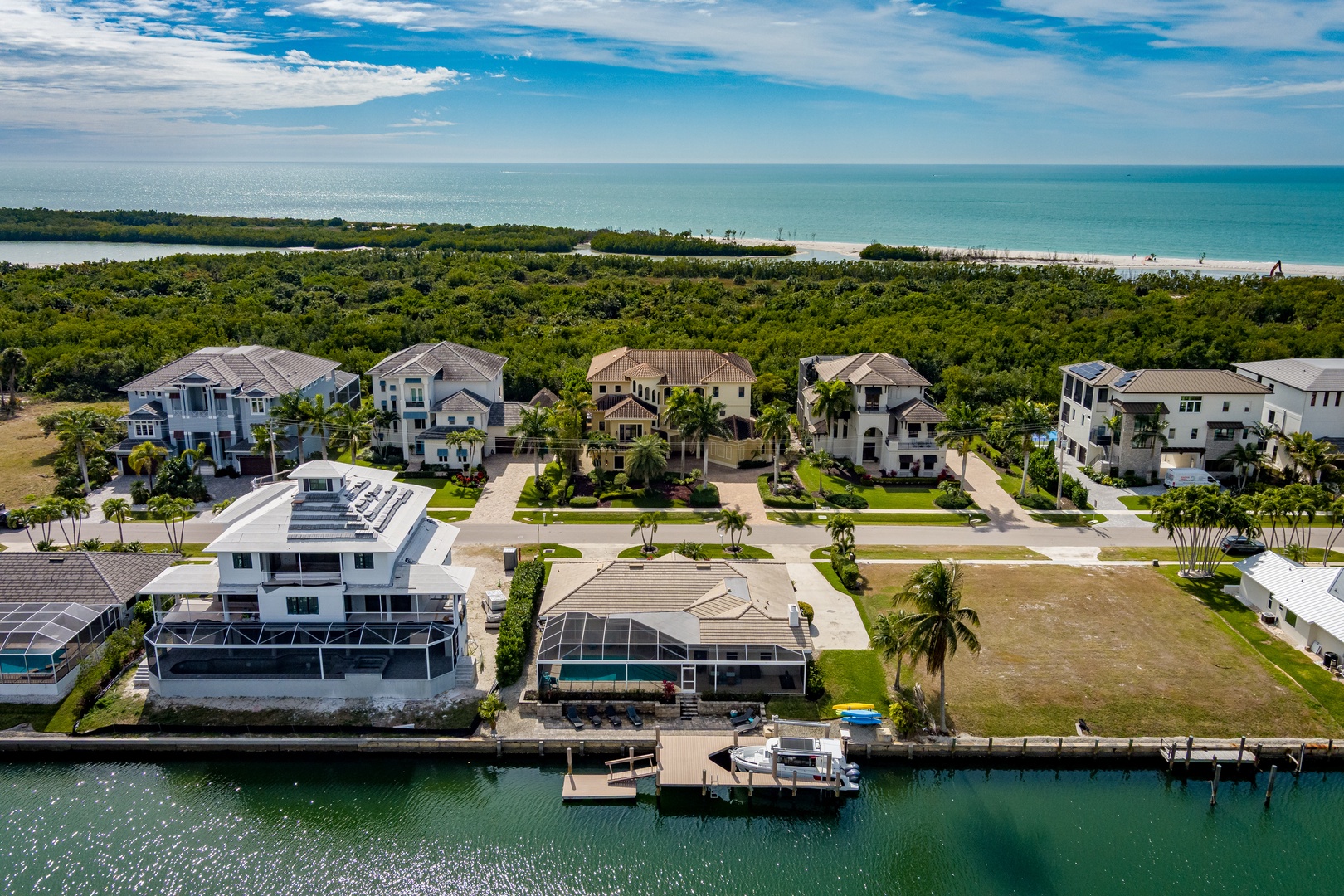 Waterfront luxury homes with private docks nestled between canal and pristine beach, surrounded by lush tropical vegetation.