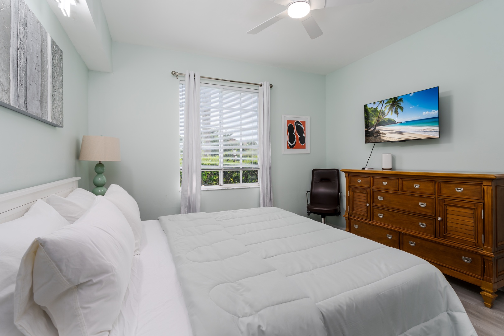 Relax in your serene bedroom with calming coastal colors, a plush bed, and a ceiling fan to keep you cool. A welcoming space for restful sleep and peaceful mornings.