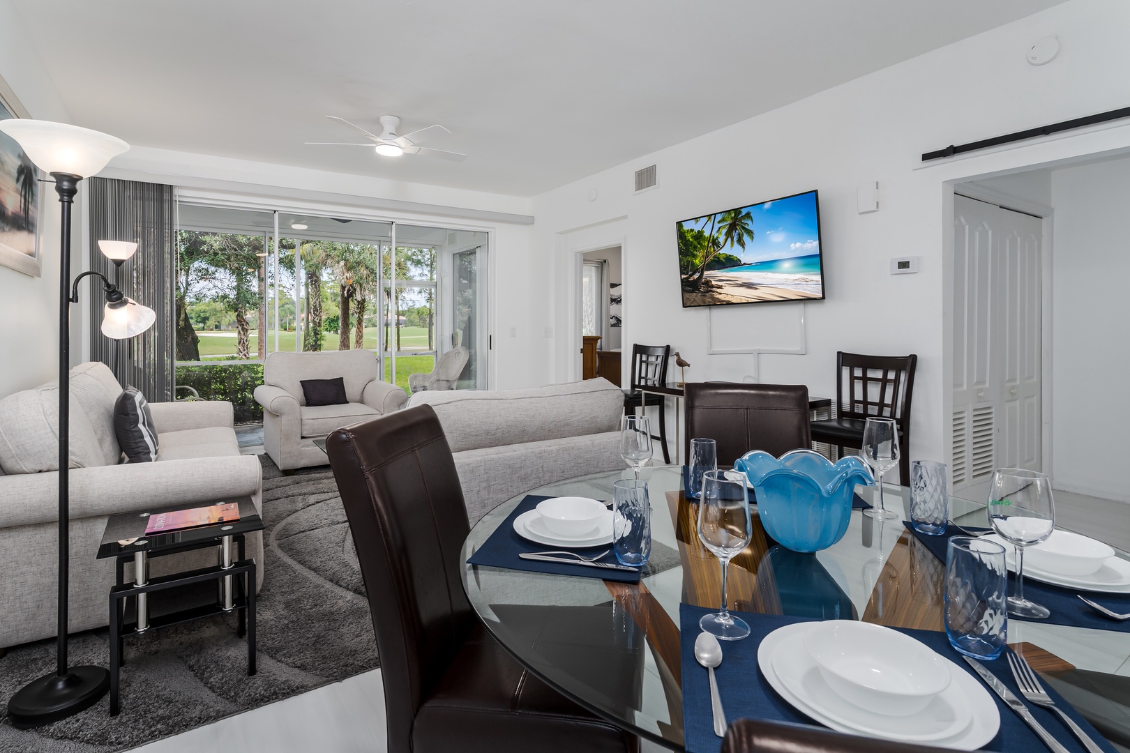 Bright, airy space where you can enjoy a meal at your elegant glass dining table, relax on the plush sofa, and unwind while gazing at lush green views through expansive sliding glass doors.
