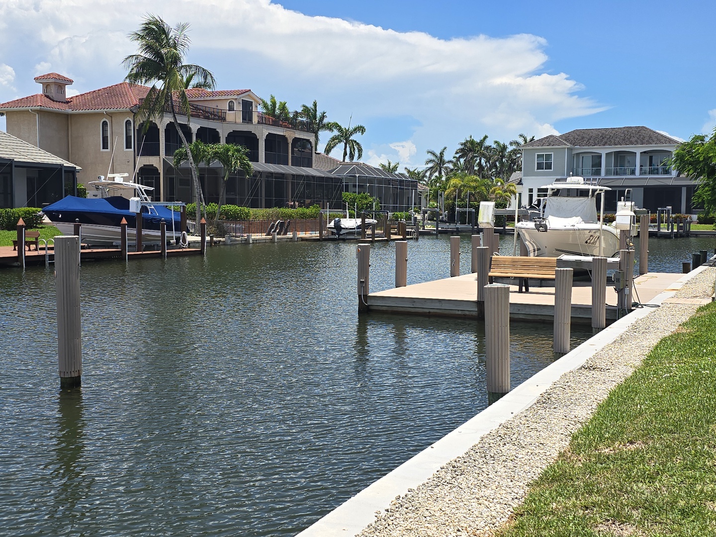 Waterfront canal community with luxury homes, private docks, and boats under sunny Florida skies with palm trees.