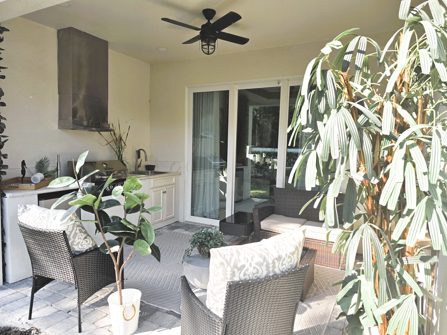 Unwind in your private covered patio with tropical plants, outdoor kitchen, and comfortable seating perfect for morning coffee or evening relaxation.