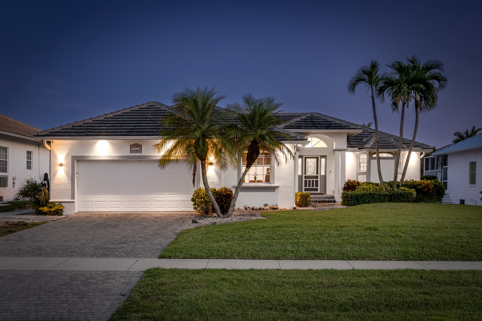Elegant single-story home with tropical landscaping and garage, located in a quiet residential neighborhood with palm trees and pristine landscaping.