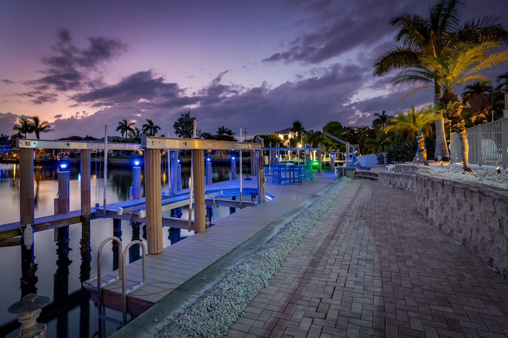 Waterfront property featuring boat docks with blue accent lighting, palm trees, and illuminated buildings set against a colorful evening sky—an ideal arrival scene for your coastal getaway.
