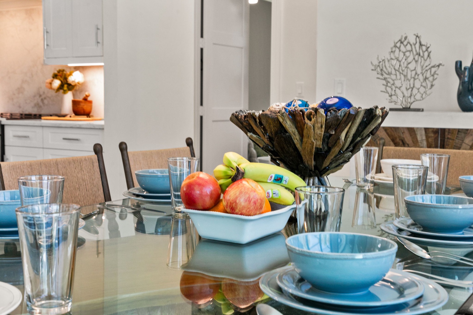 Your dining table is set with coastal-inspired blue bowls and fresh fruit, ready for shared meals that feel like home. The open kitchen beckons in the background, inviting you to cook and gather.