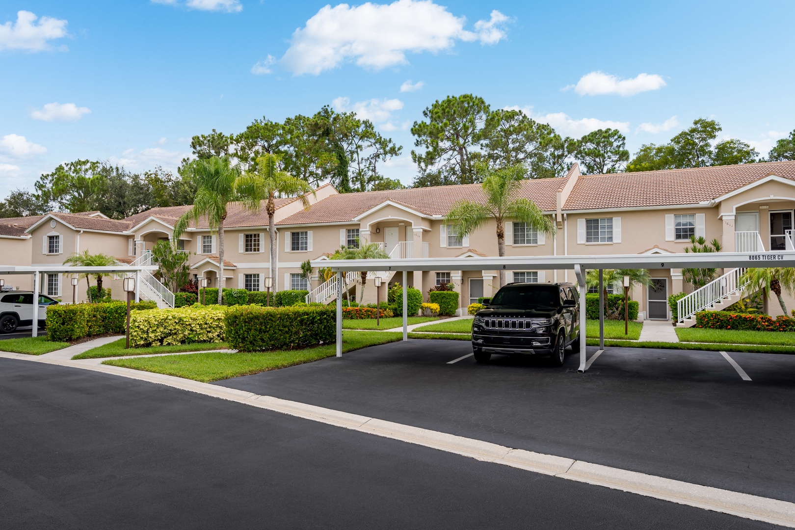 A welcoming community setting with covered parking and lush tropical landscaping, nestled in a peaceful residential neighborhood beneath mature trees.
