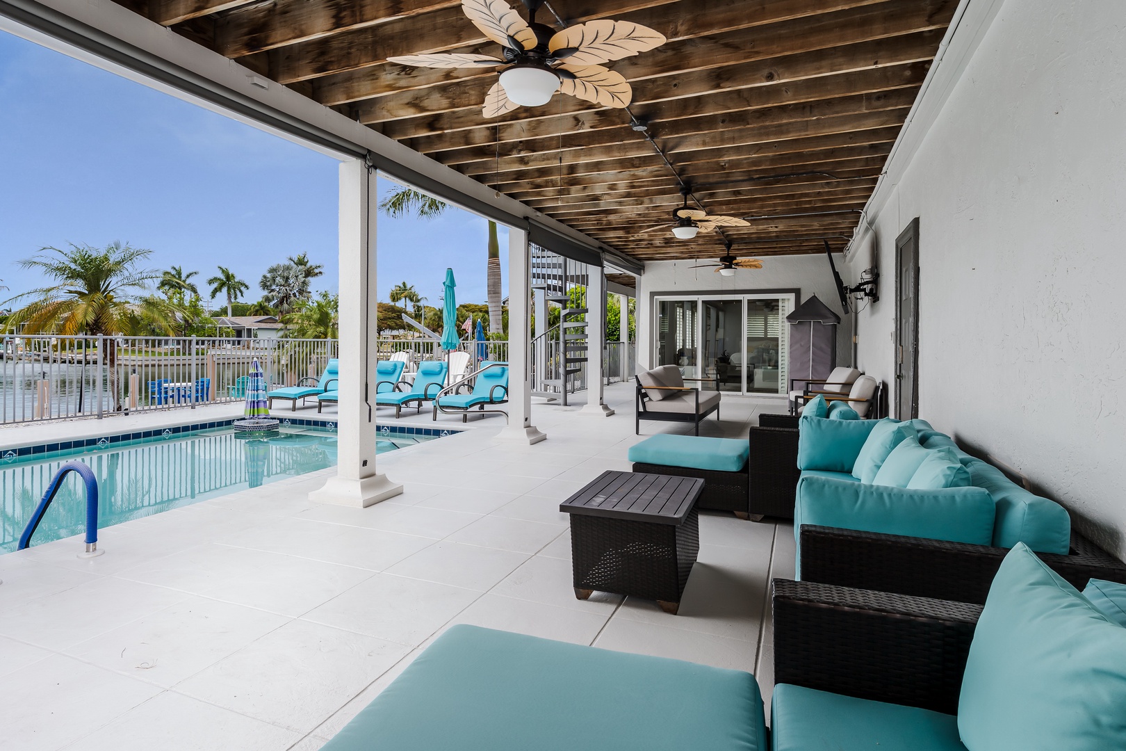 Unwind on your private covered patio with vibrant turquoise seating and tropical ceiling fans. Step out to your pool, surrounded by lush palms and refreshing waterfront views.