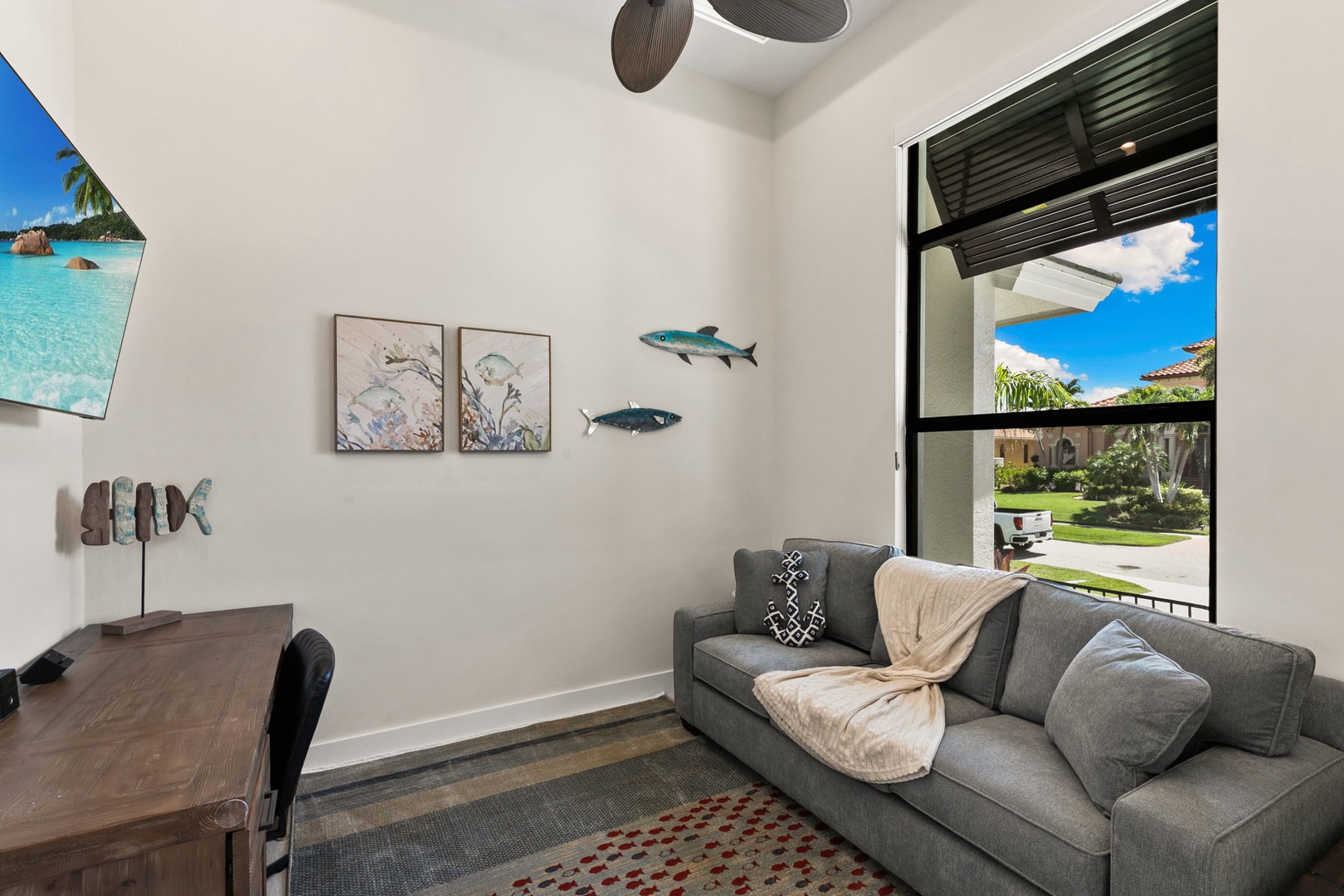 Relax in your cozy sitting area with plush seating and coastal decor, where natural light fills the space and a view of the neighborhood awaits just beyond the window.
