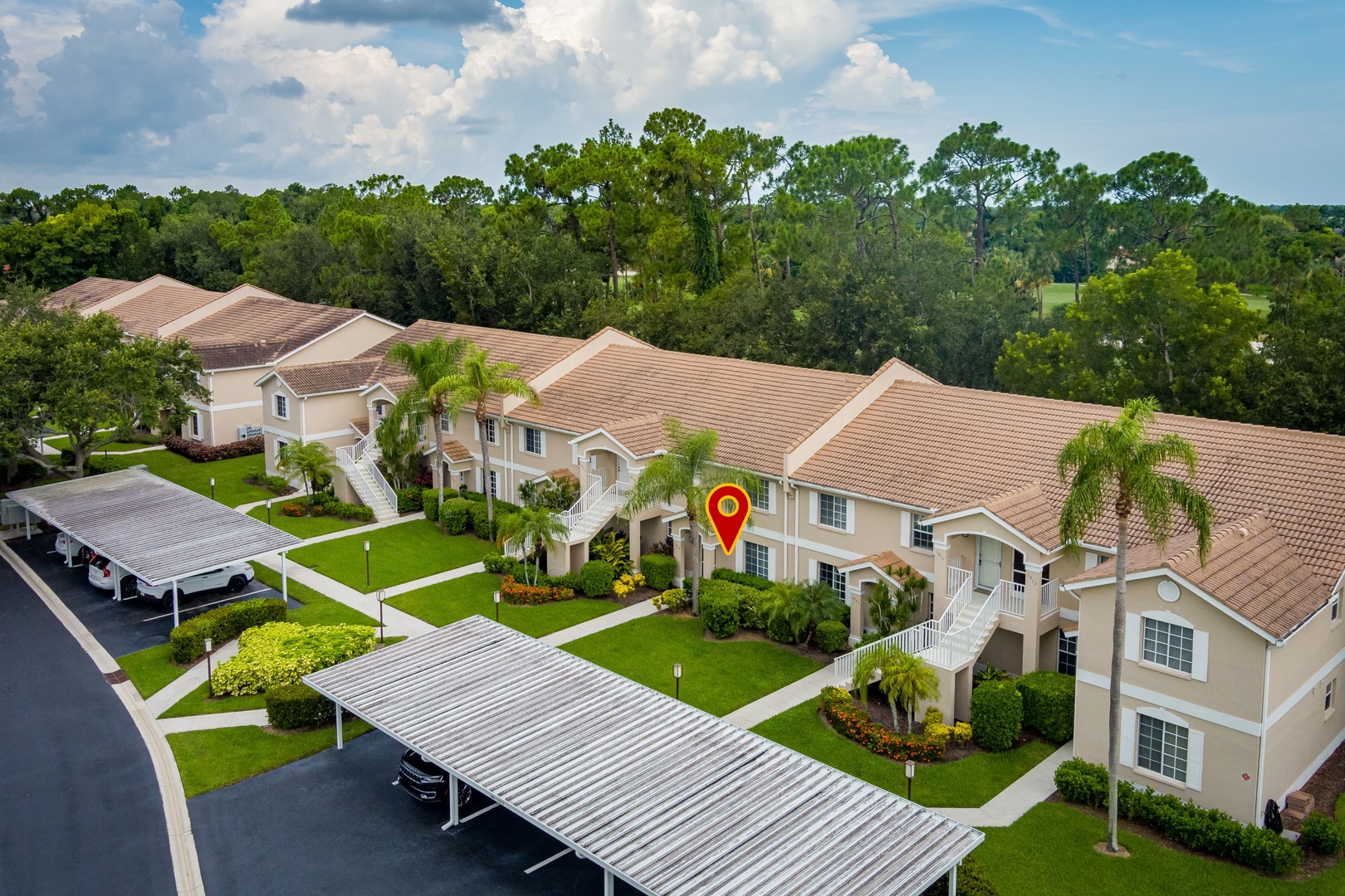 Aerial view of a residential community featuring Mediterranean-style buildings with terra cotta roofs, surrounded by lush tropical landscaping and mature trees with a golf course backdrop.