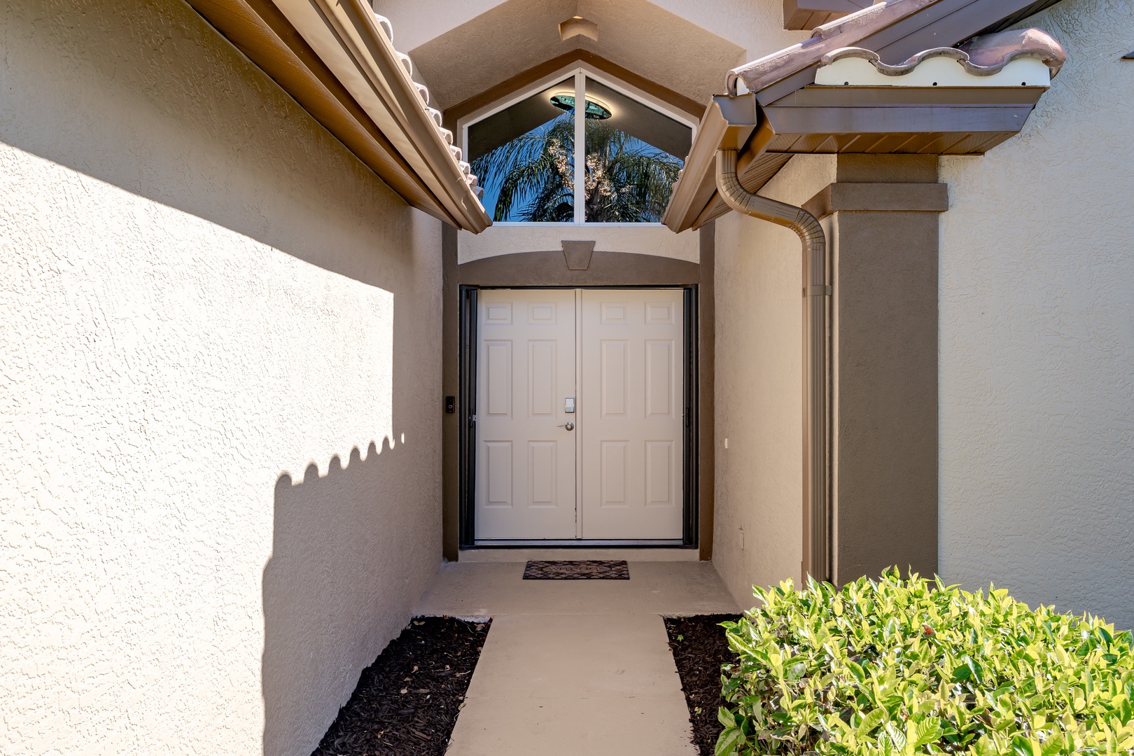 A welcoming entrance with Mediterranean-style architecture features white stucco walls, tile roof, and tropical landscaping for your arrival.