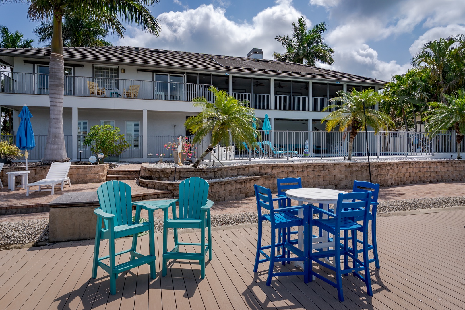 A sunny outdoor gathering space with vibrant seating beneath swaying palms, perfect for sipping morning coffee or enjoying sunset cocktails with friends.