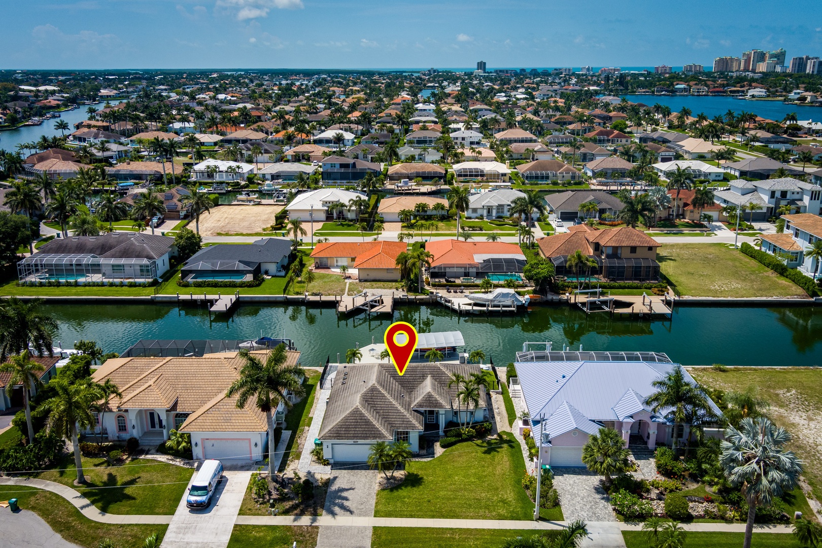 Aerial view of a waterfront vacation rental in a coastal neighborhood with private dock access, surrounded by palm-lined streets and neighboring homes along peaceful canals.