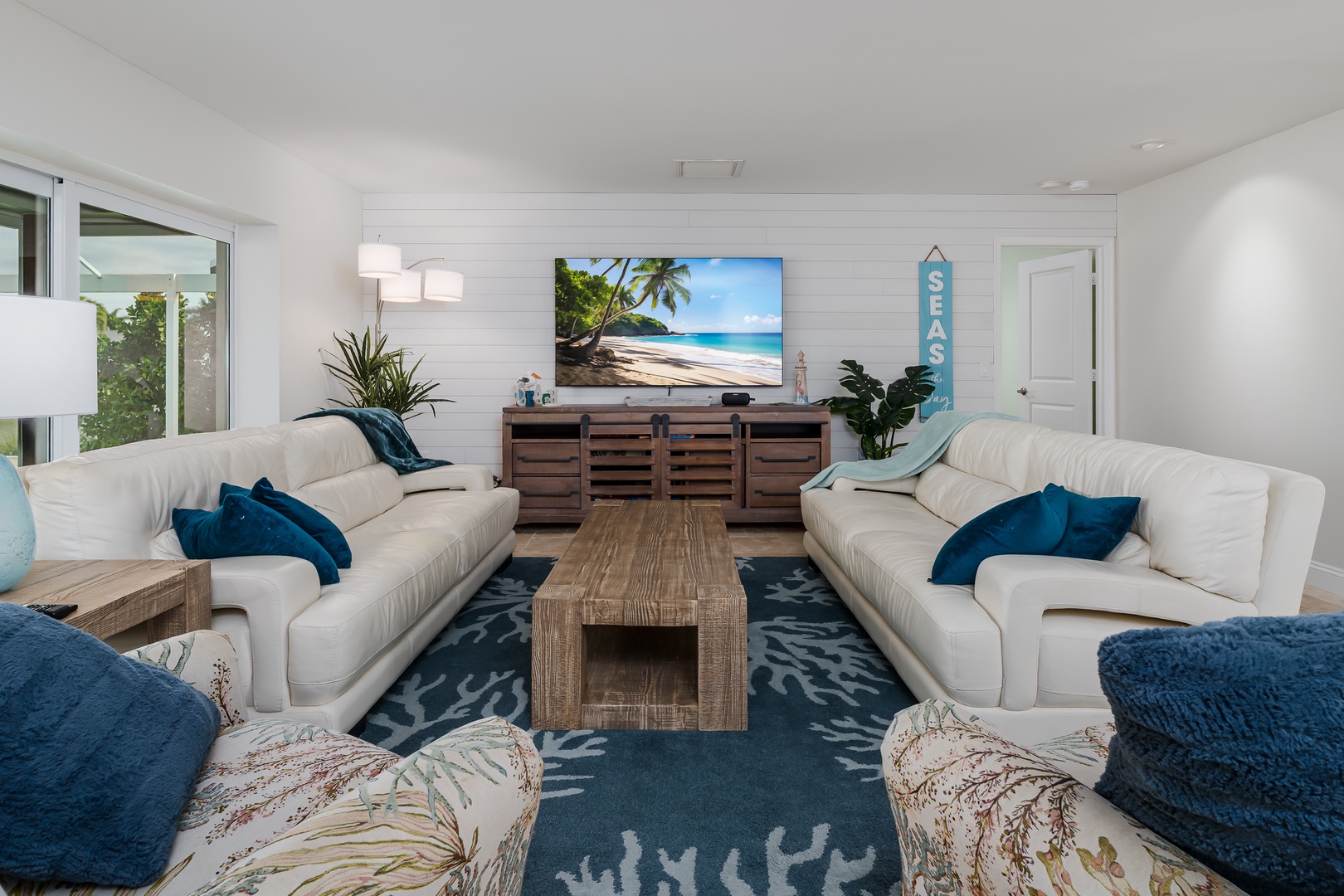 Sink into plush white sofas with ocean-blue accents as tropical vibes fill your coastal retreat.
