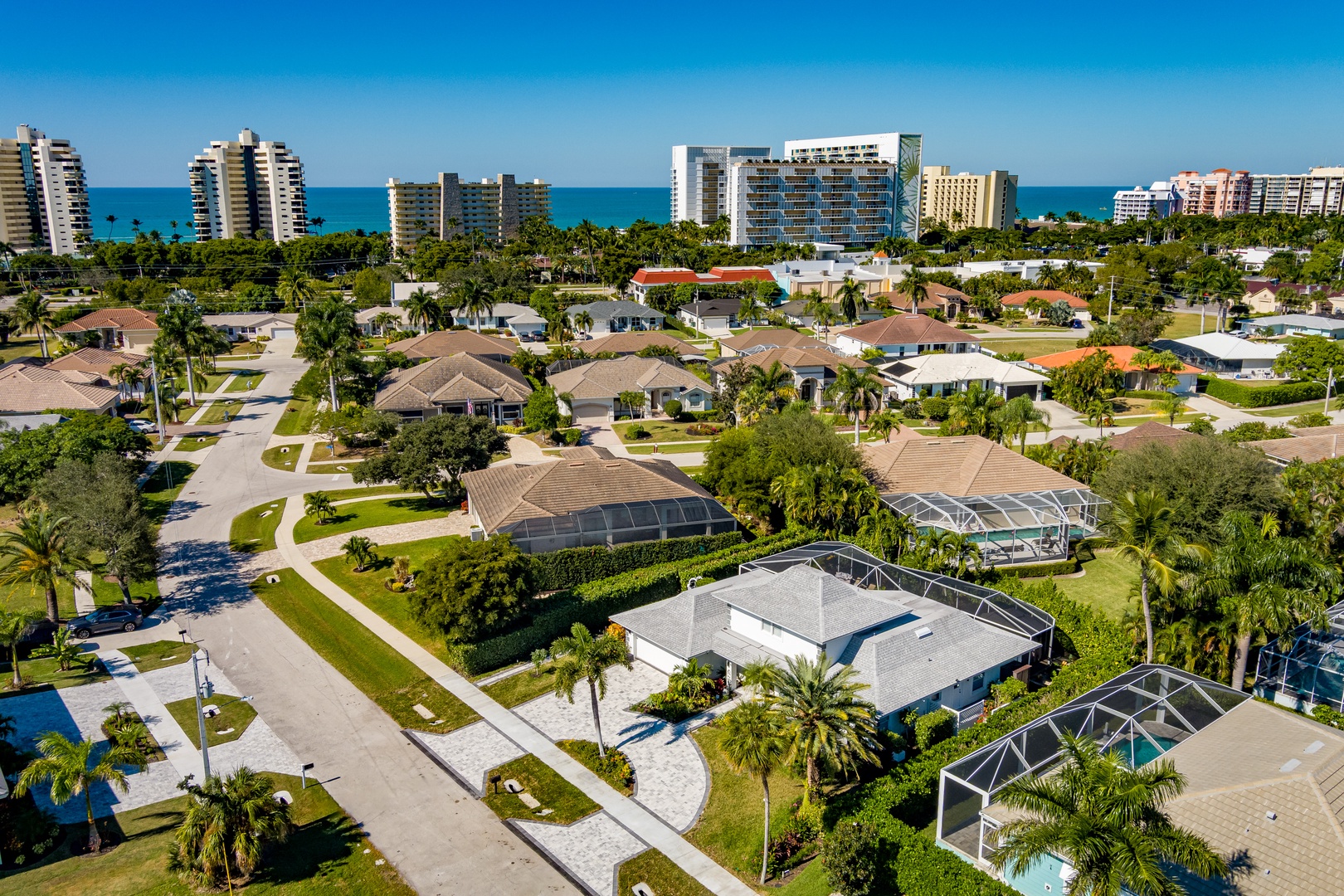 Aerial view of a peaceful coastal neighborhood with resort-style homes, lush tropical landscaping, and pristine beaches just moments away.