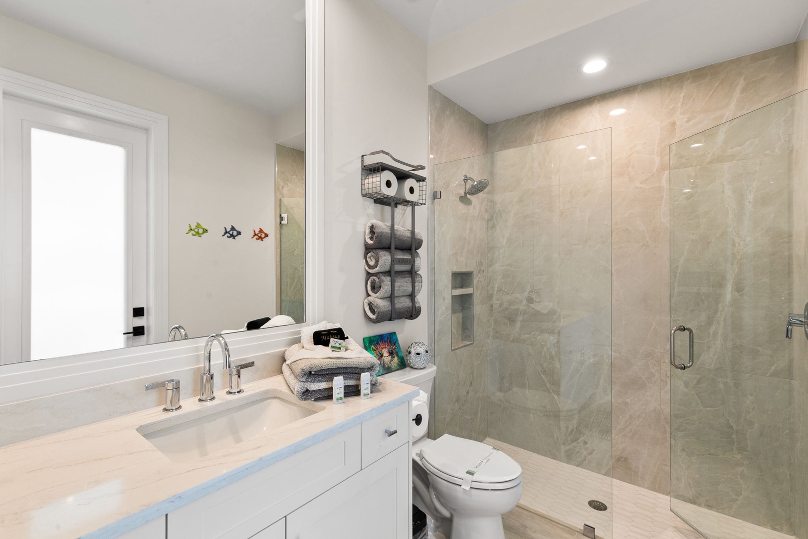 Step into your modern bathroom featuring a spacious walk-in shower with elegant marble-look tile, a bright vanity with ample counter space, and thoughtful touches like fresh towels and coastal décor to welcome you.