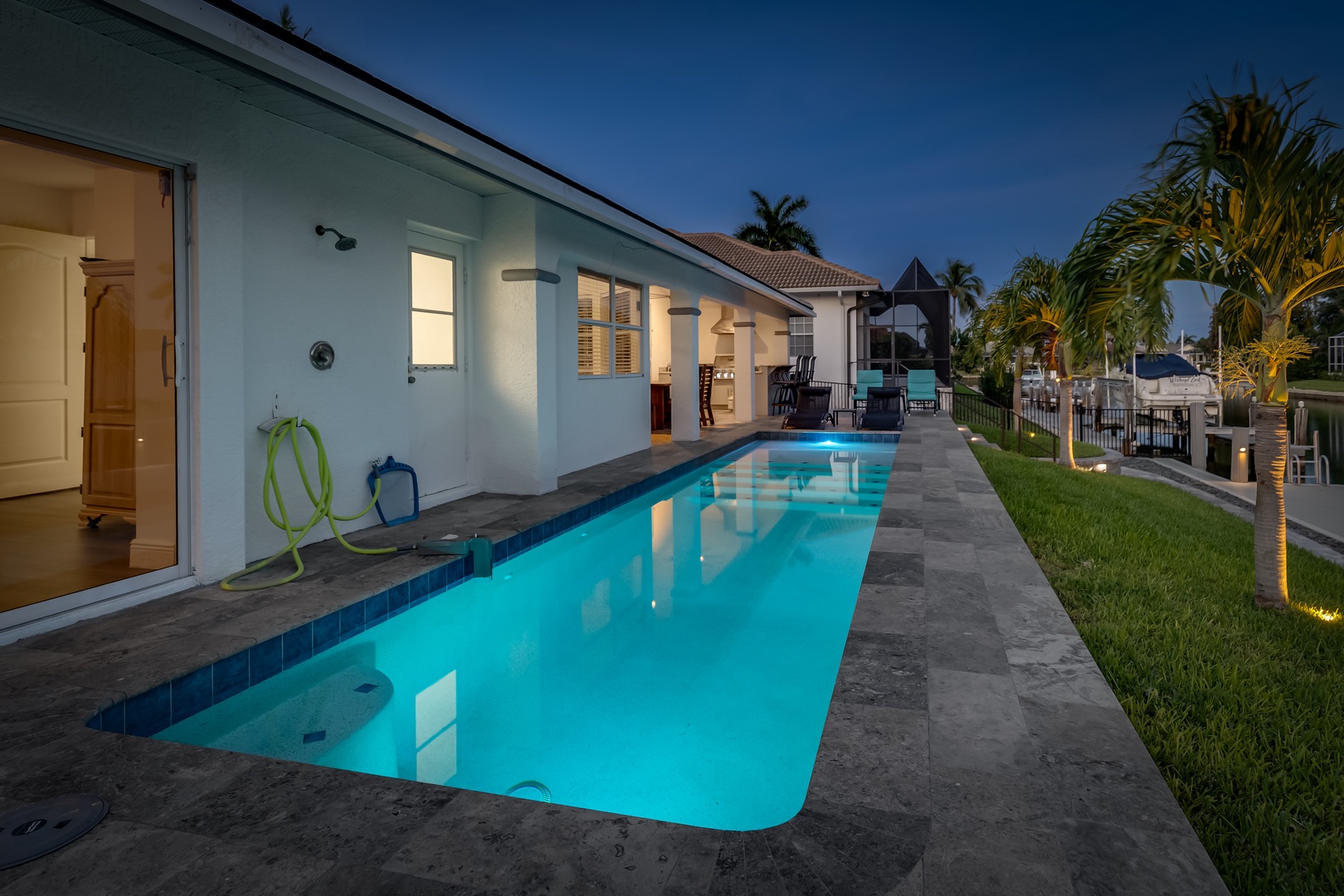 This waterfront property features a sleek lap pool lit beautifully at twilight, bordered by palm trees and a spacious deck overlooking a canal with boat access nearby.