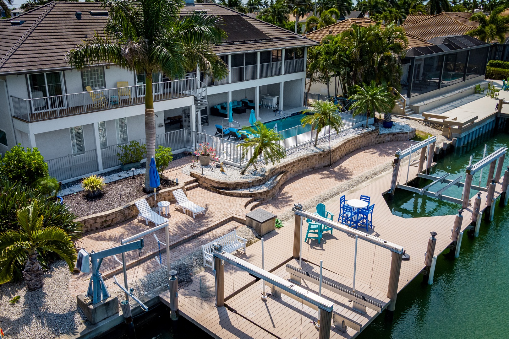 This waterfront property features a multi-level design with direct canal access and private docks. The tropical landscape includes palm trees, a pool area, and expansive outdoor spaces perfect for Florida coastal living.