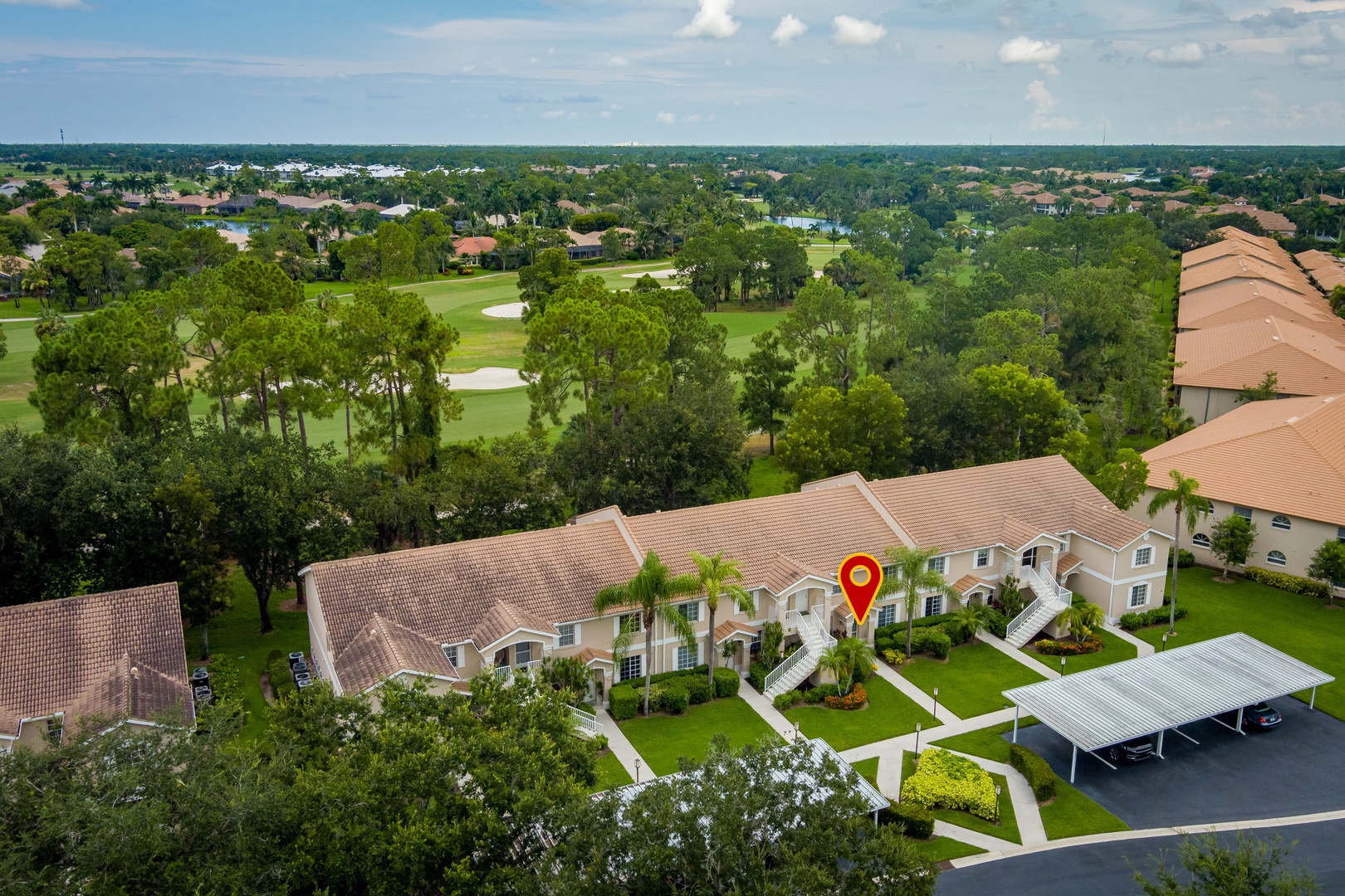 Aerial view of a residential community nestled within a lush golf course neighborhood, surrounded by mature trees and tropical landscaping under a bright Florida sky.