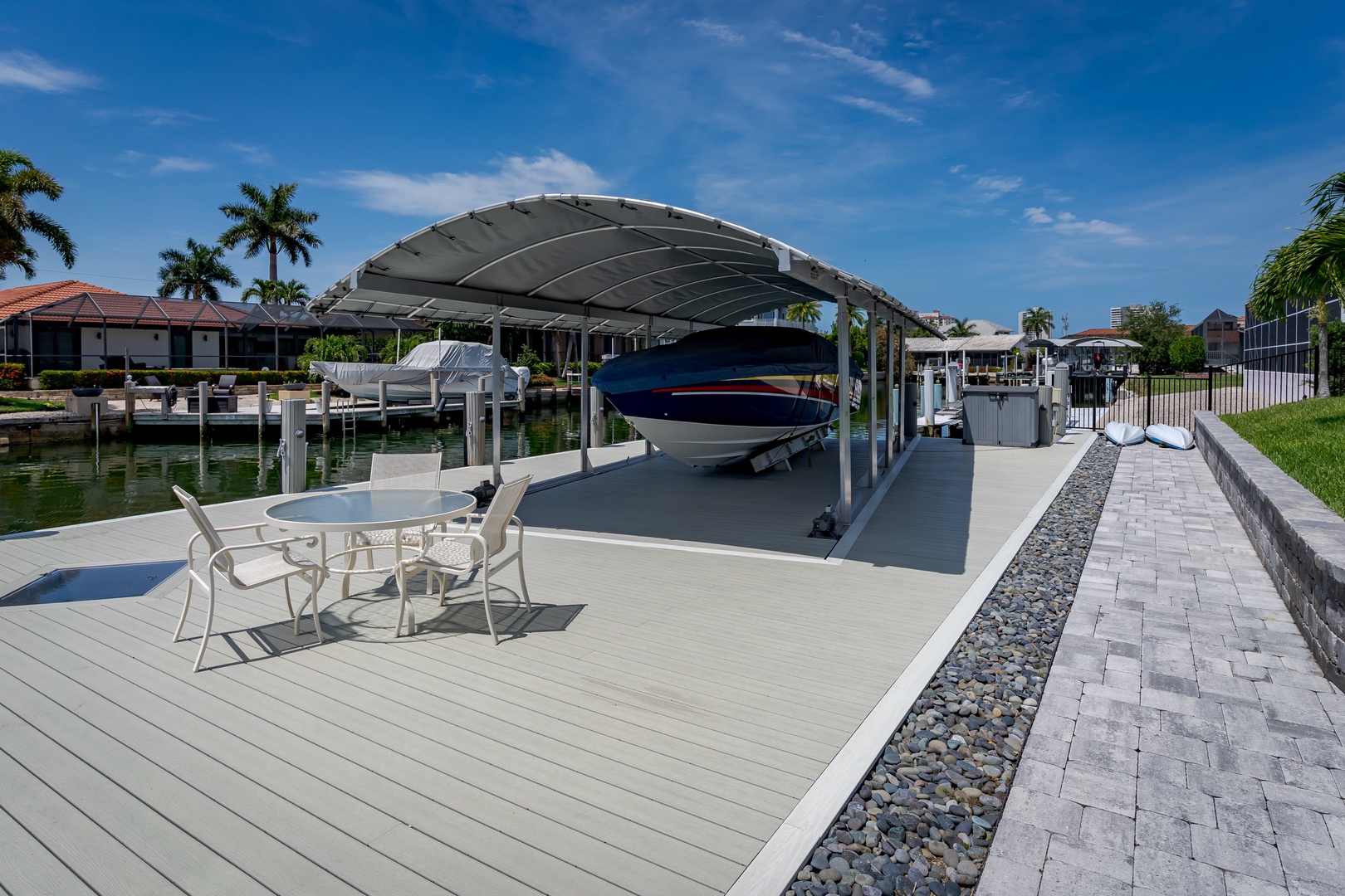 Private dock with boat slip and covered canopy sits on a peaceful waterfront canal, surrounded by palm trees and waterfront homes in a tranquil residential area.