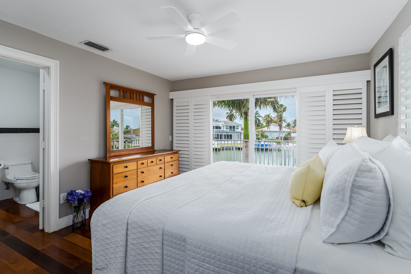 Wake up to serene waterfront views framed by swaying palms. Your bright, peaceful bedroom features a plush bed, en-suite bath, and shuttered windows that invite in coastal breezes.
