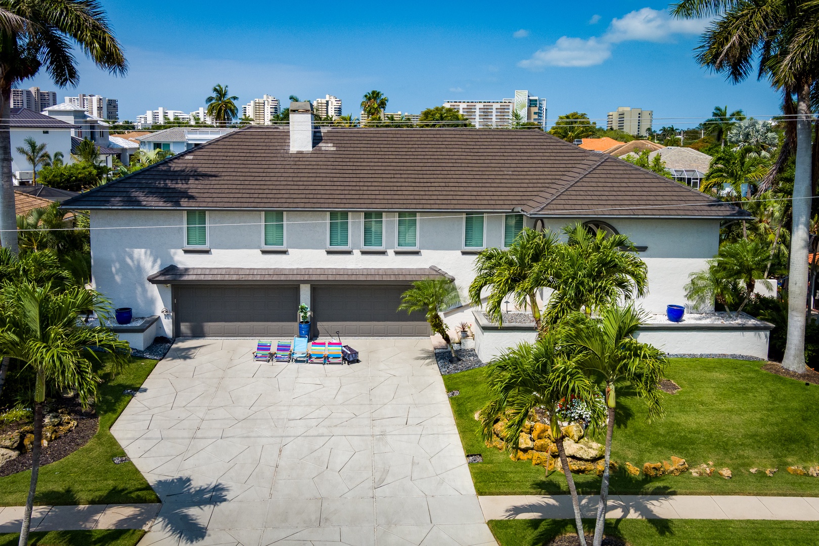 Spacious two-story vacation home features a modern exterior with tropical landscaping, lounging area, and ample parking, all set in a sunny residential neighborhood with coastal vibes.