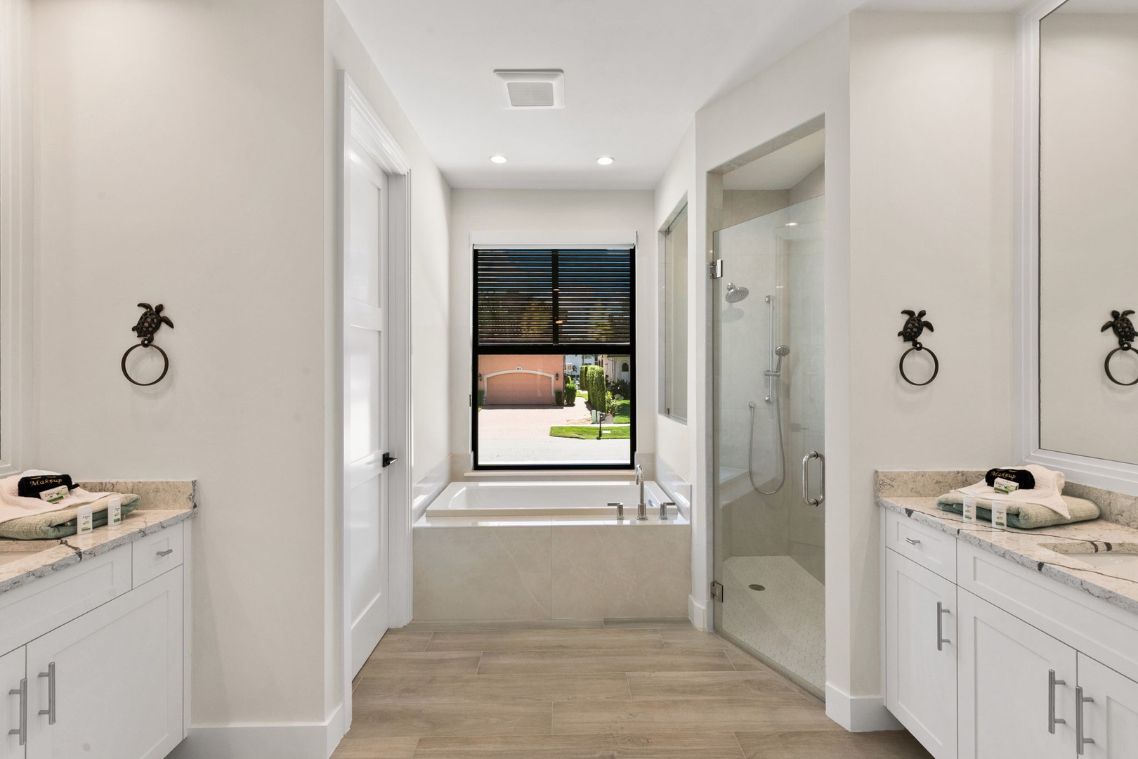 This bright and elegant bathroom features dual vanities, a soaking tub with a garden view, and a glass-enclosed shower—perfect for starting your day refreshed and relaxed.