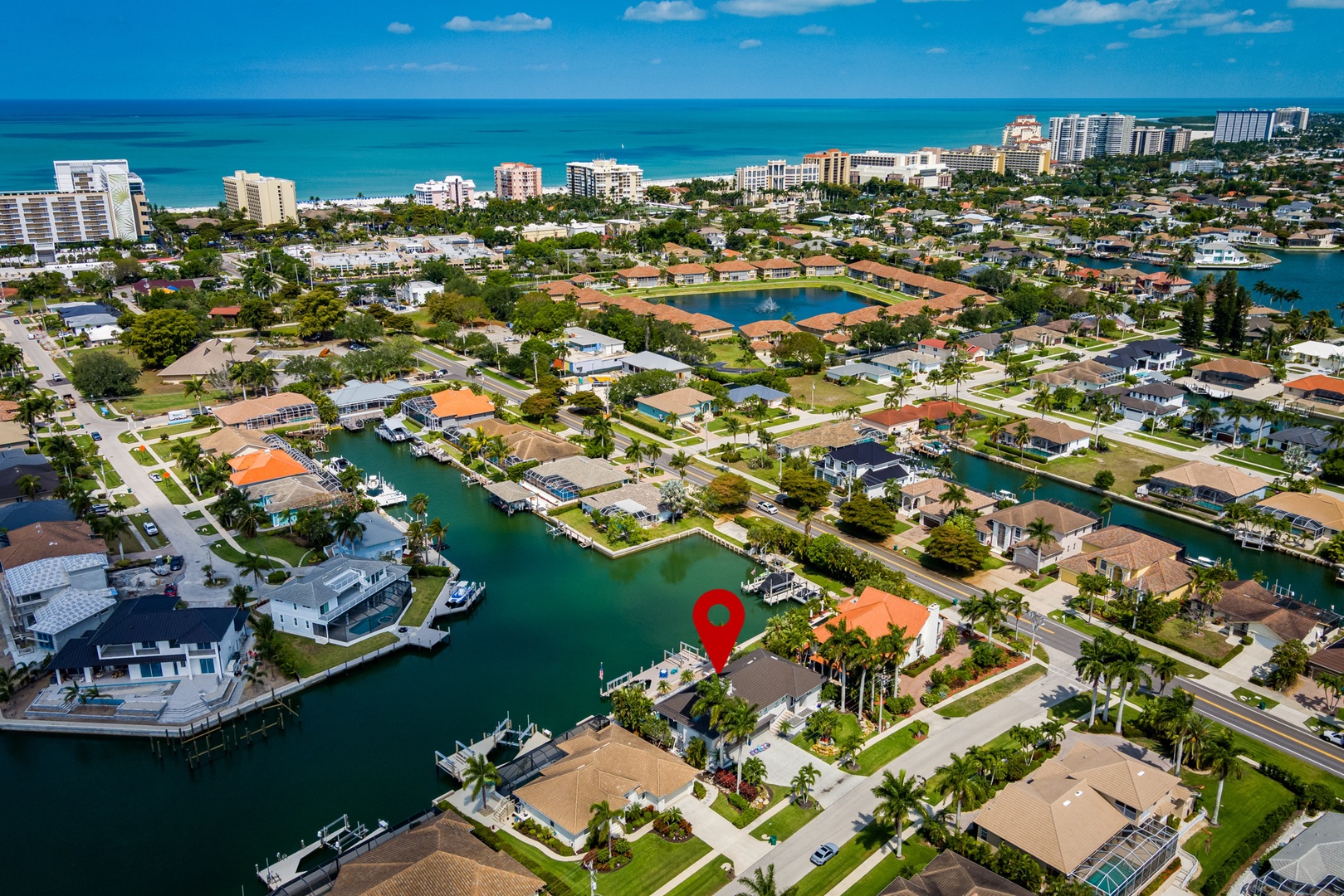 Aerial view of a waterfront vacation rental in a serene coastal neighborhood, surrounded by canals, palm-lined streets, and pristine beaches, offering direct access to ocean and city amenities.