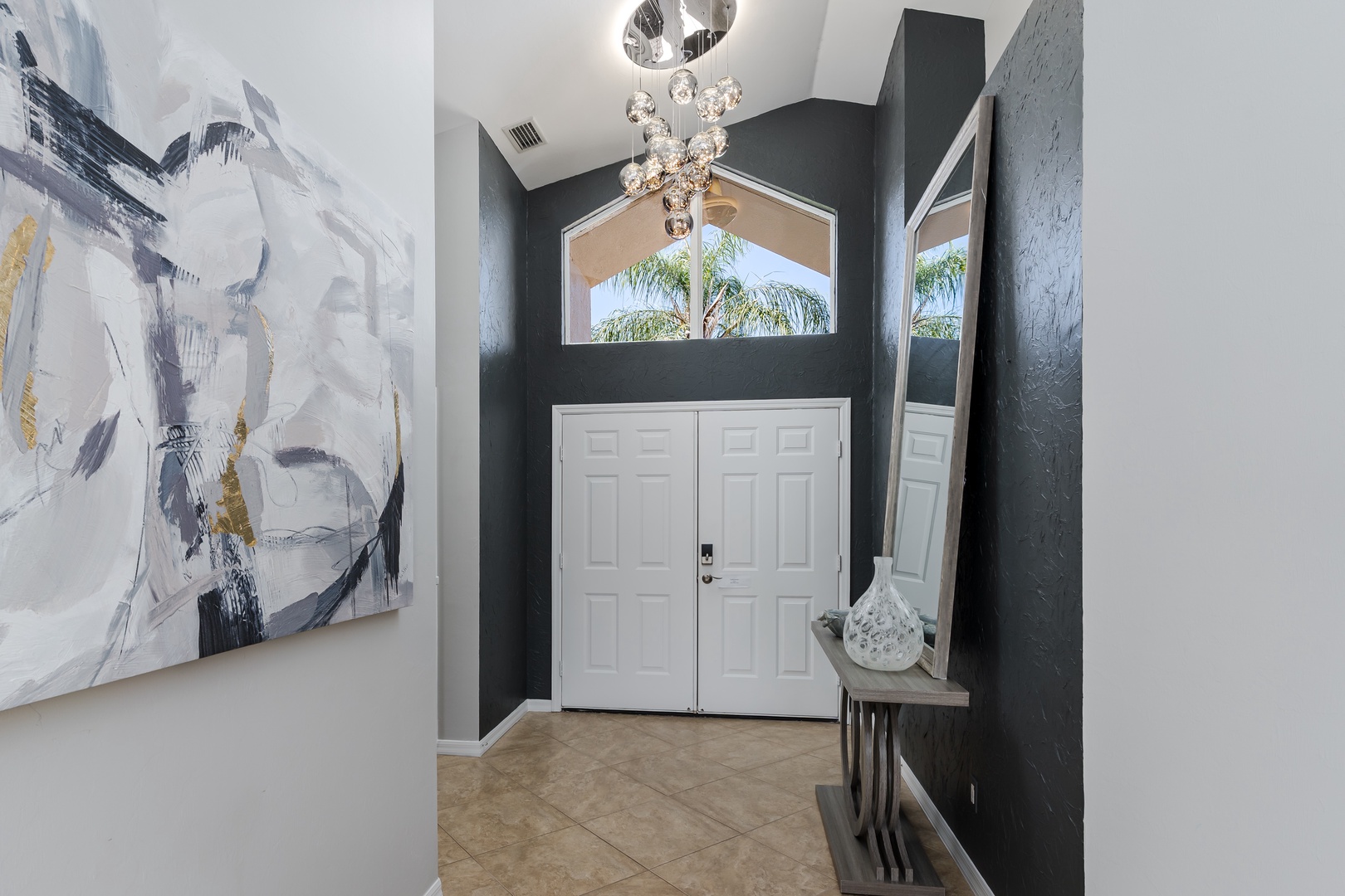 You'll be welcomed by this stunning entryway with modern art, elegant lighting, and peaceful palm tree views through the glass doors.