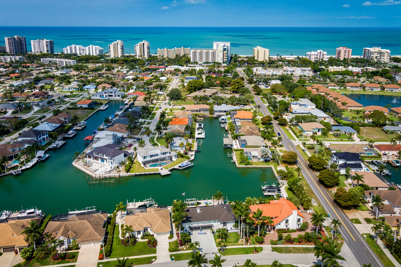 Aerial view of a waterfront neighborhood featuring canal-access homes, private docks, lush landscaping, and nearby beaches along the turquoise coastline.