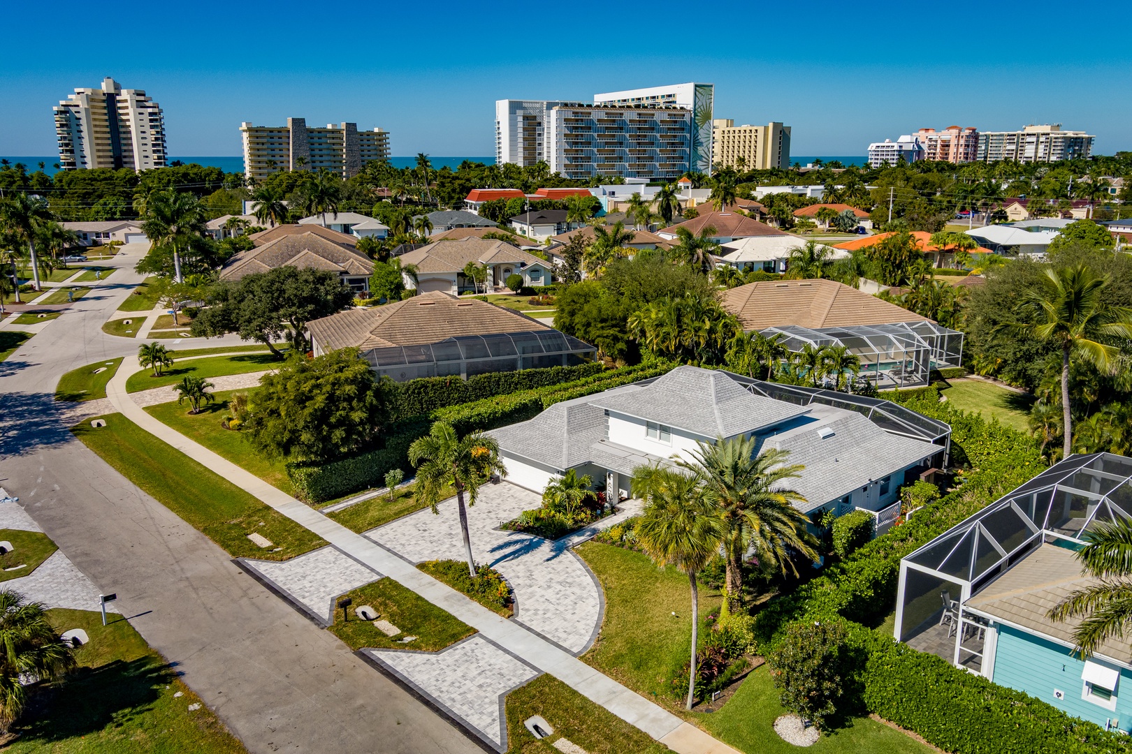 Aerial view of tropical beachside neighborhood with palm trees, resort hotels, and residential properties near the coast.