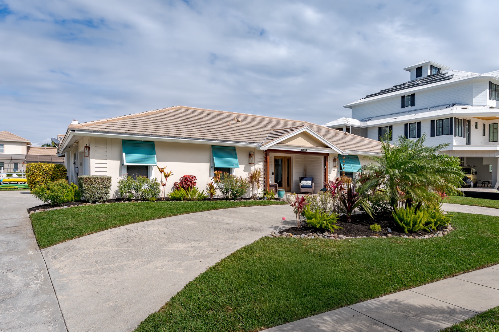 A charming single-story home with turquoise shutters and tropical landscaping in a peaceful residential neighborhood.
