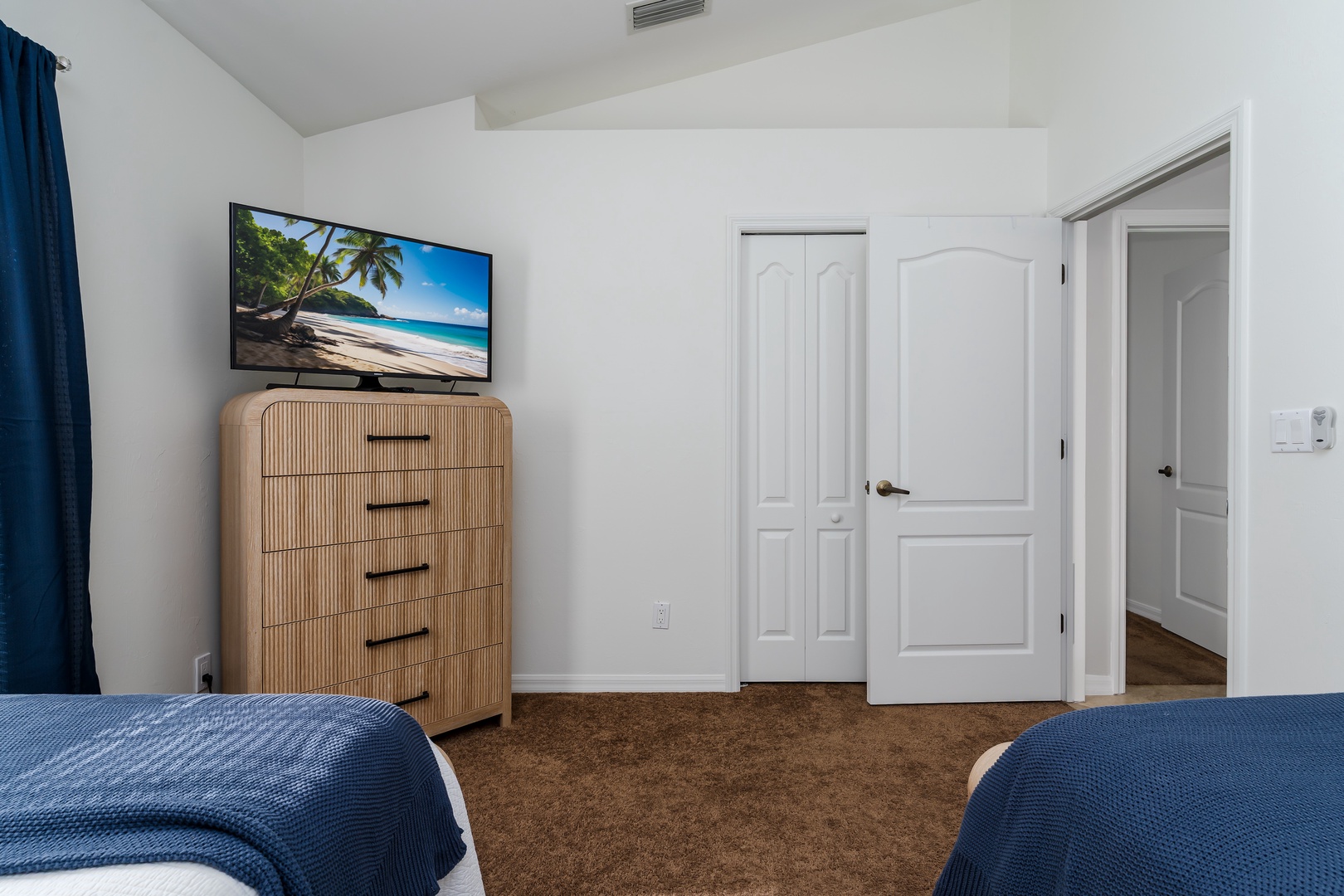 Unwind in your stylish bedroom featuring a large TV, cozy blue accents, and ample storage in the elegant wooden dresser.