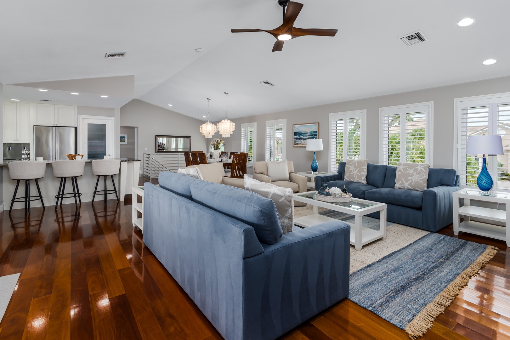 Sunlight streams through plantation shutters, illuminating your open-plan living space where coastal blues meet gleaming hardwood floors. High vaulted ceilings and modern fixtures create an airy retreat perfect for unwinding together.