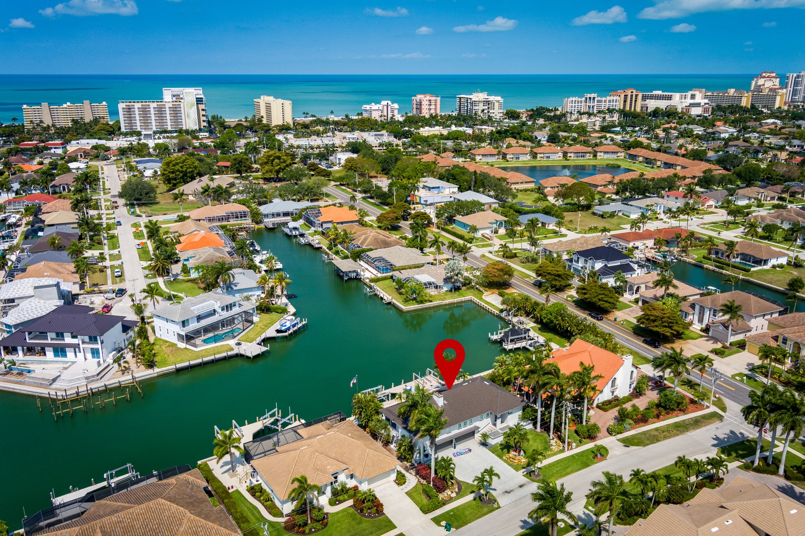 Aerial view of a waterfront neighborhood featuring canal-front homes with private docks, lush landscaping, and ocean views in the distance. The property is nestled in a tranquil coastal community.
