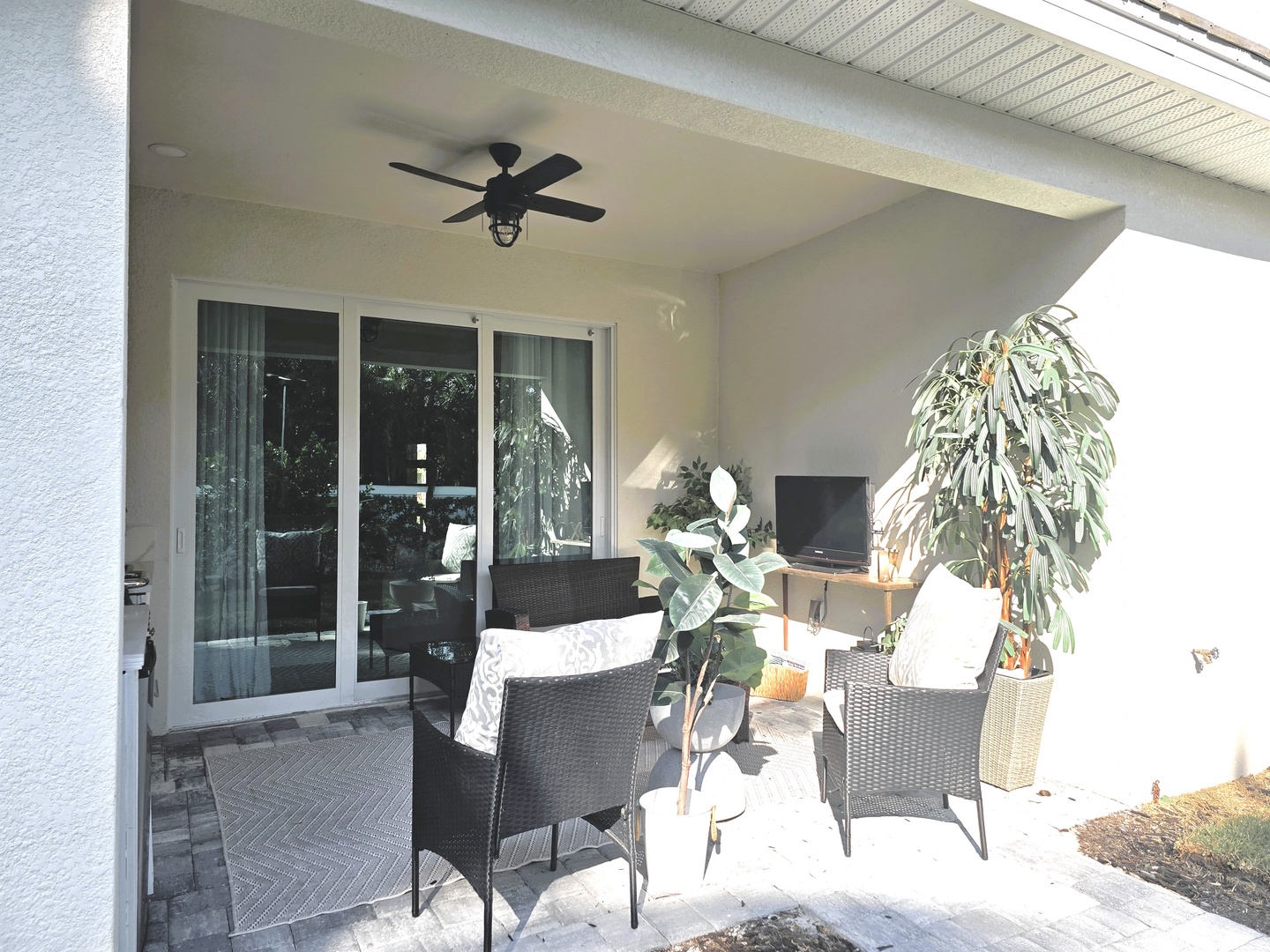 Relax on your private covered patio with comfortable seating, ceiling fan, and tropical plants creating your perfect outdoor retreat.