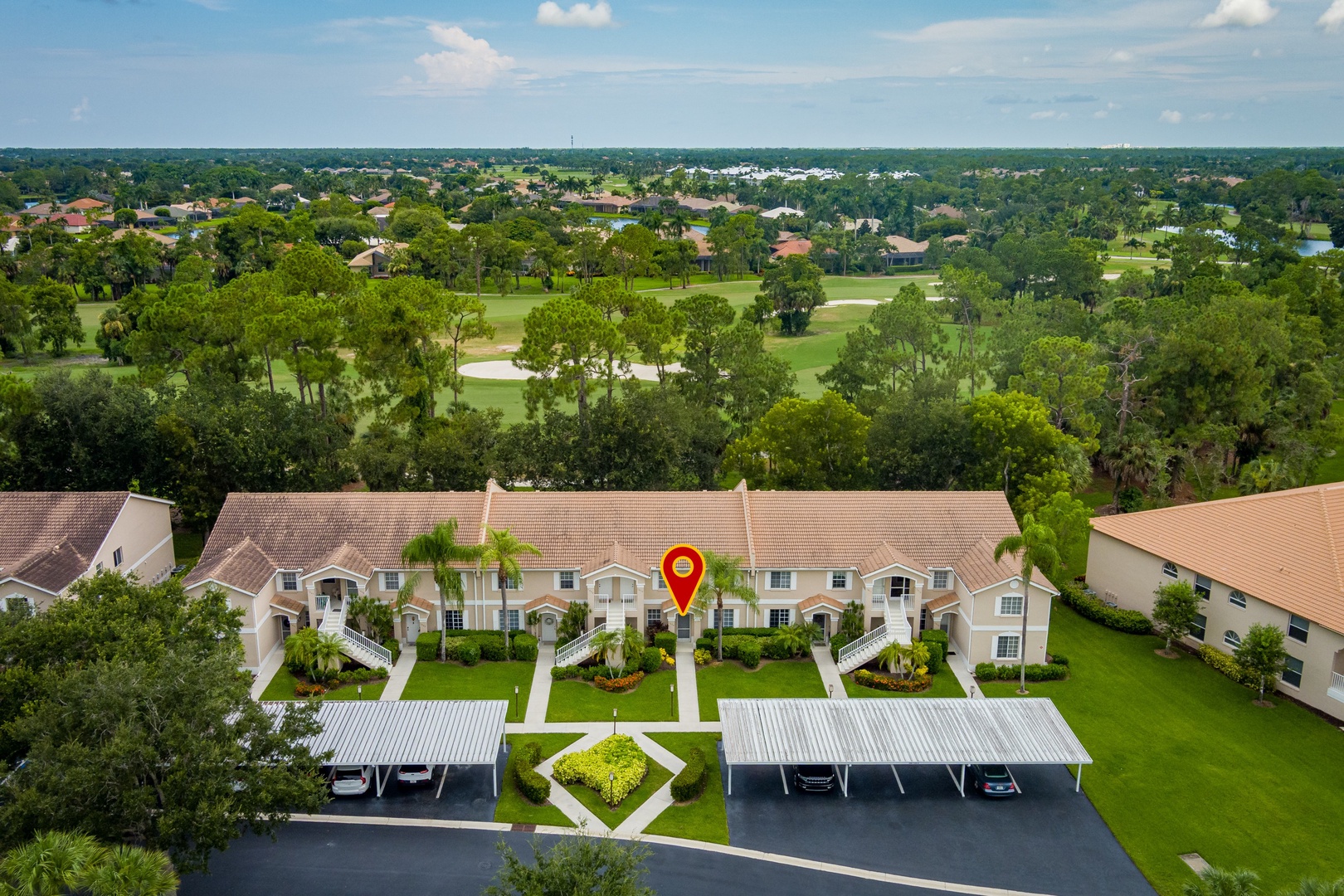 Aerial view showing the property nestled within a lush golf course community, surrounded by mature trees and landscaped grounds with covered parking.