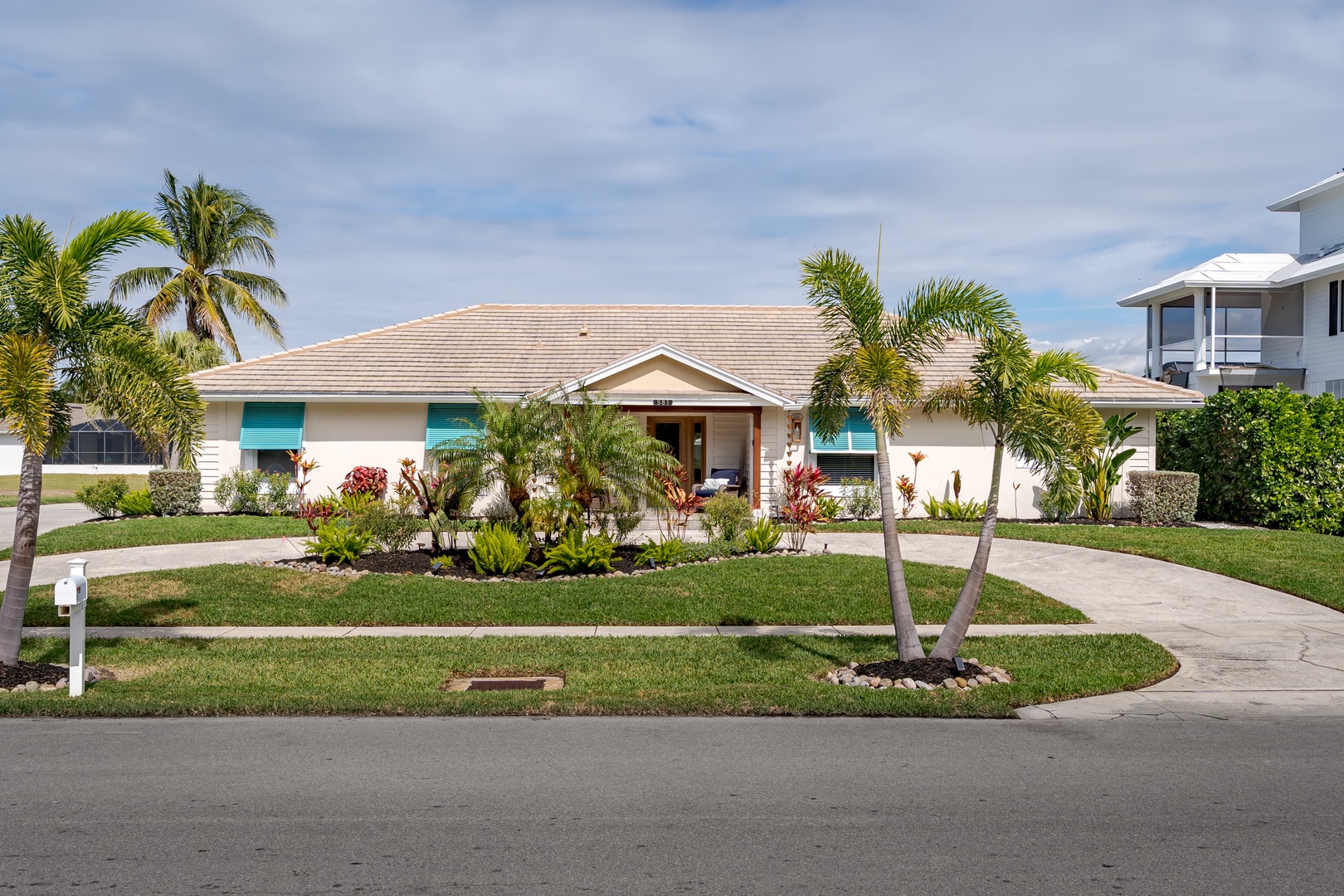 Charming single-story home featuring tropical landscaping with palm trees, colorful plantings, and a welcoming entrance in a peaceful residential neighborhood.