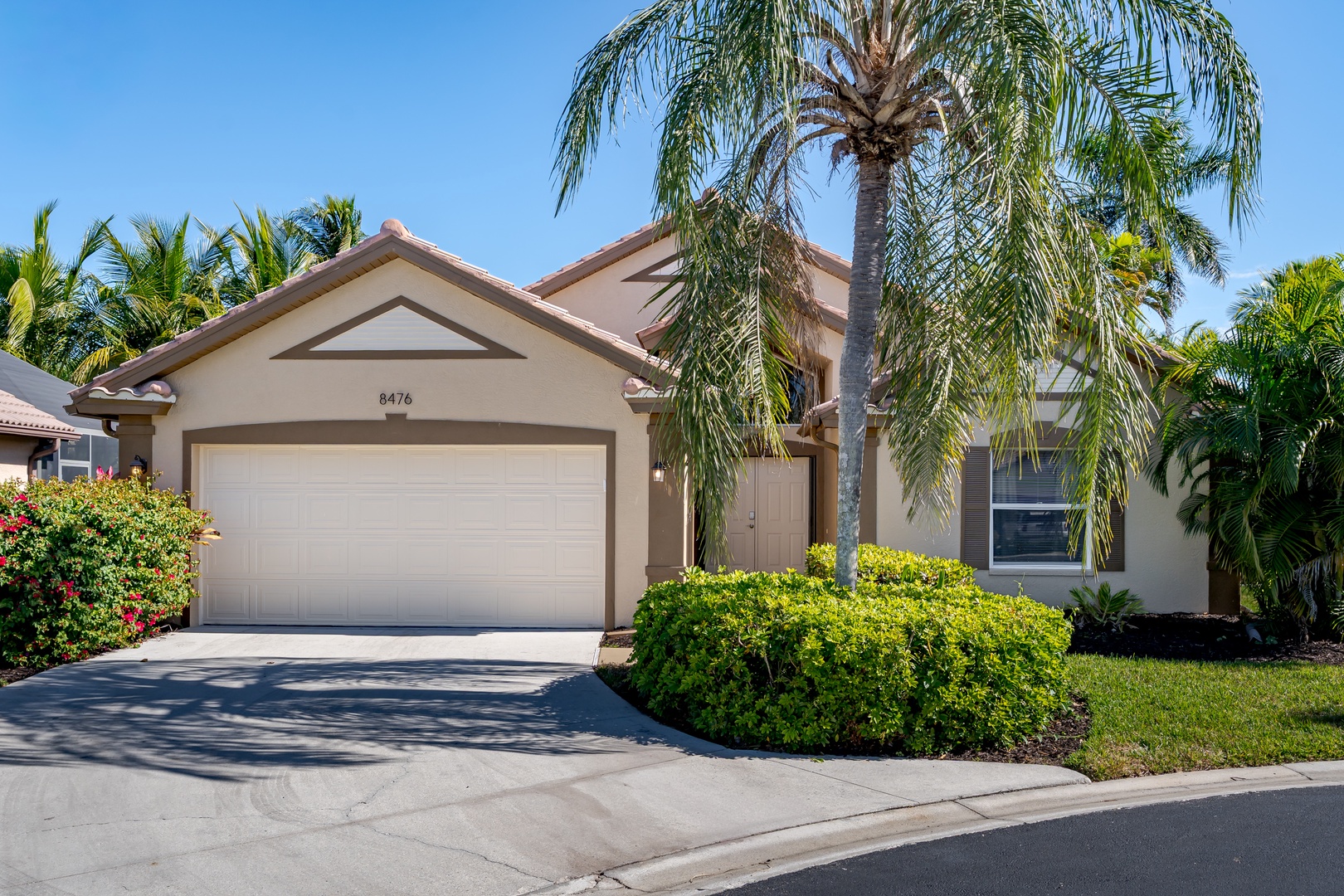Tropical single-story home with palm trees and manicured landscaping in a sunny residential neighborhood.