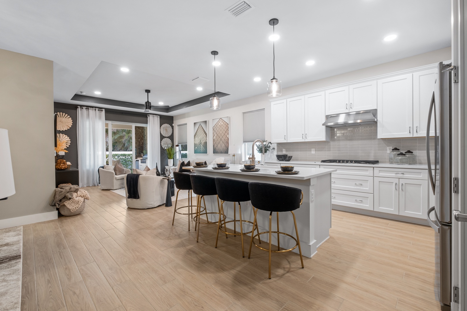 Your modern kitchen flows seamlessly into the living area, featuring white cabinets, stylish pendant lights, and a spacious island perfect for gathering.